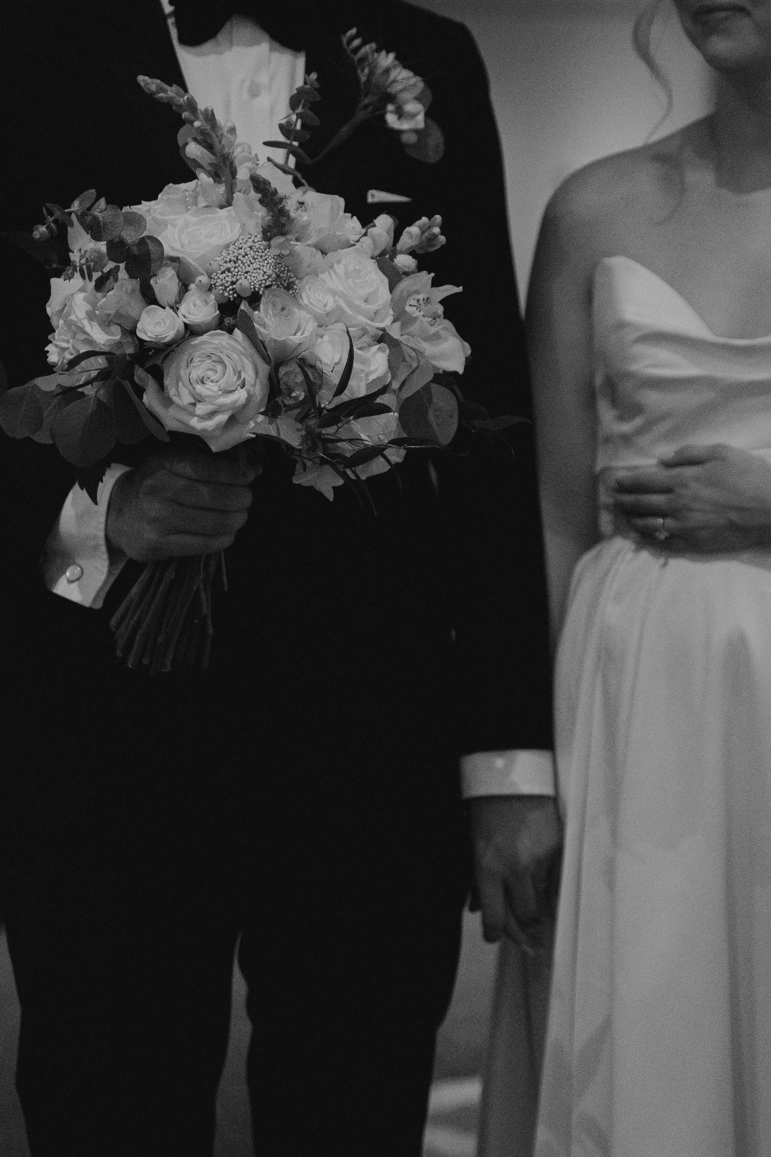Black and white detail of bridal bouquet with roses held against formal wedding attire.