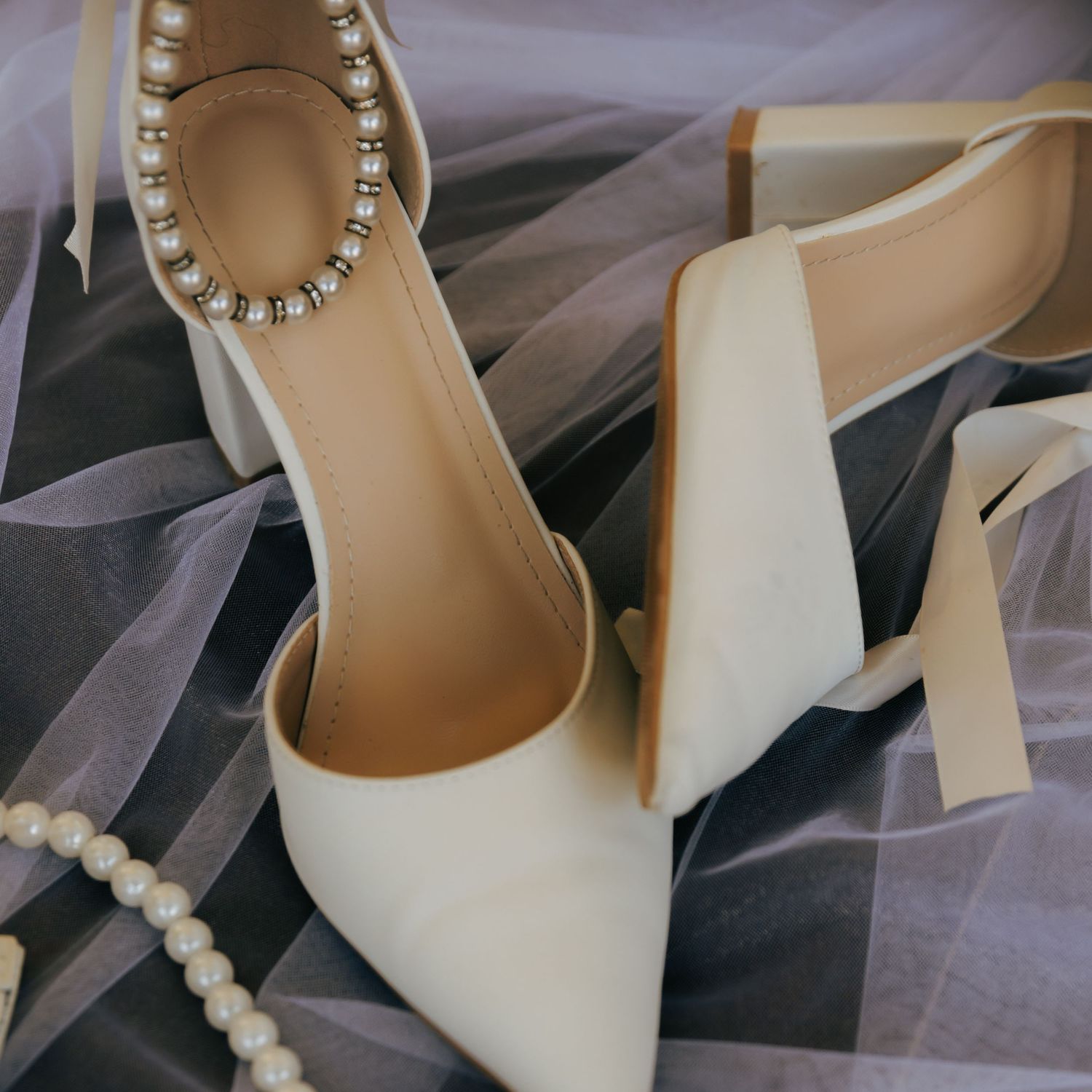 Elegant white wedding shoes with pearl ankle straps on tulle fabric.