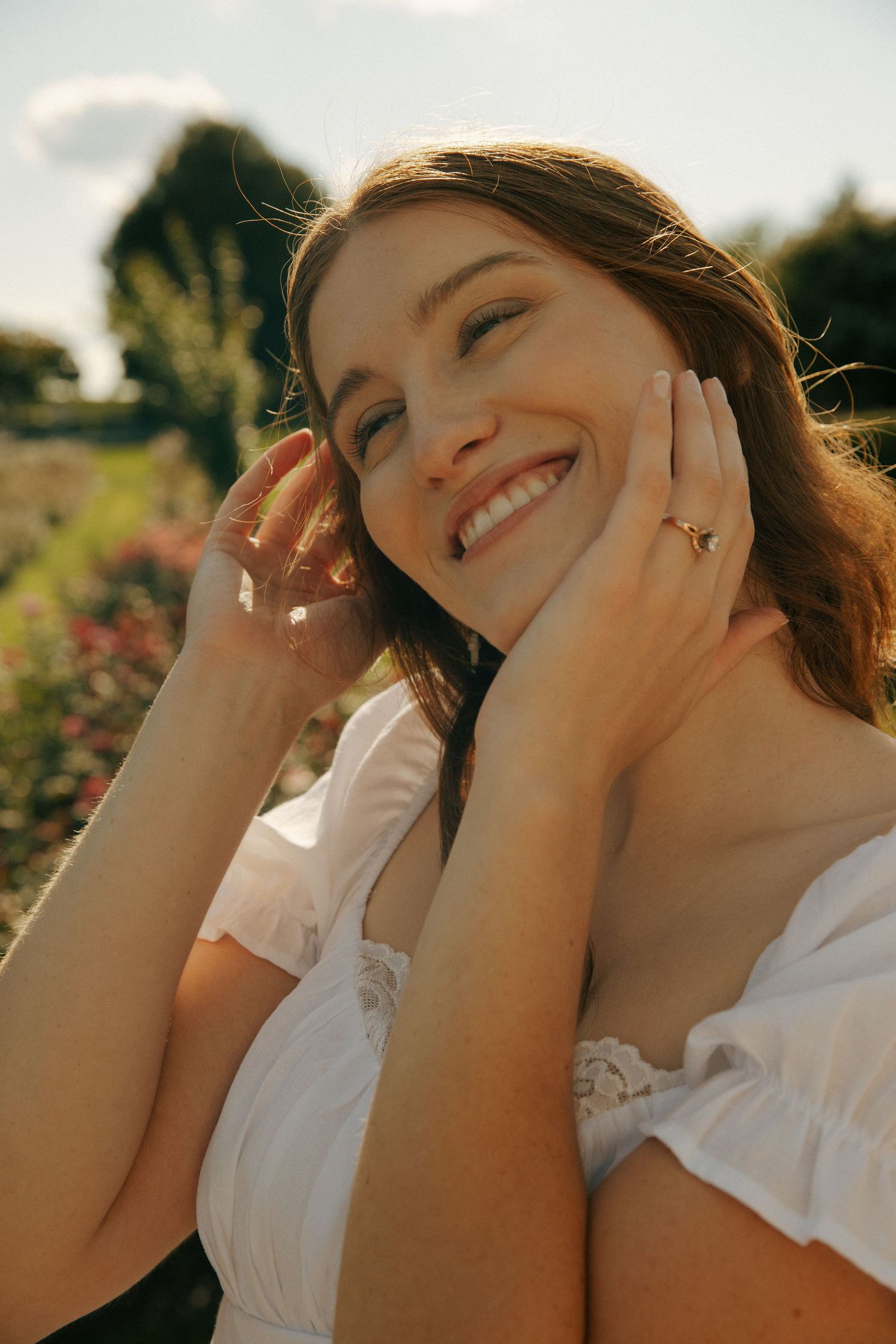 Sunlit portrait in white dress against garden background with genuine smile.