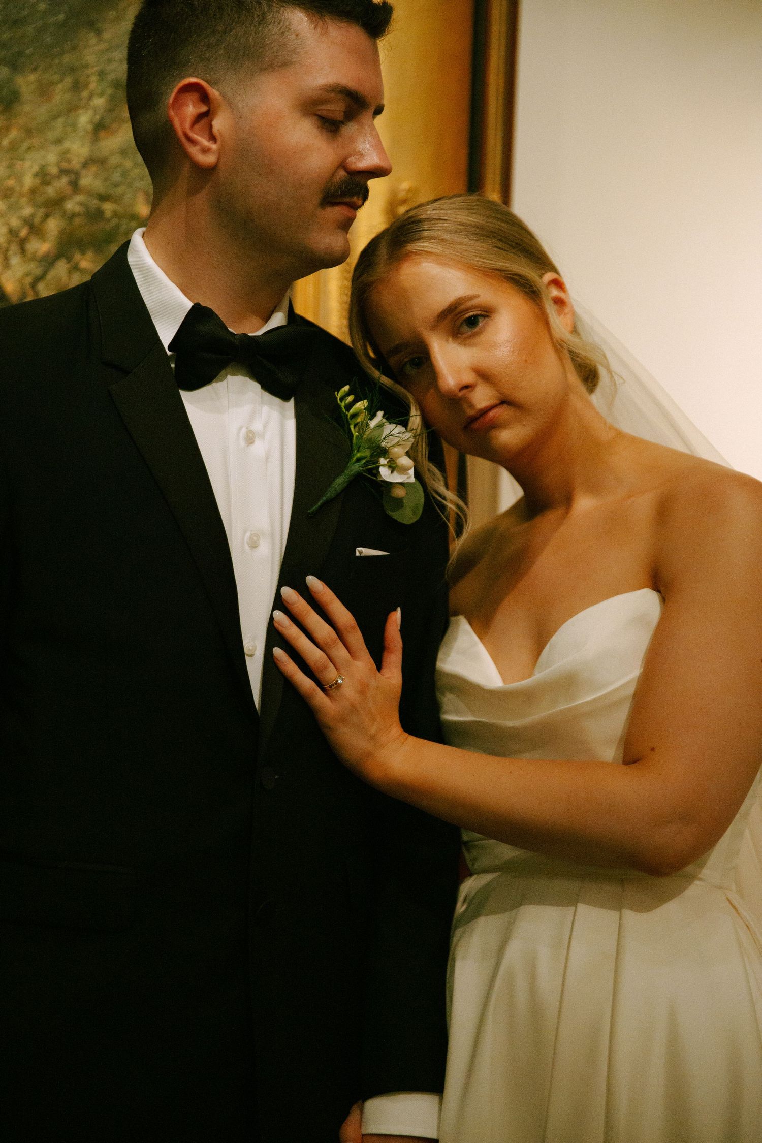 Romantic wedding portrait shows couple in intimate moment against gallery wall.