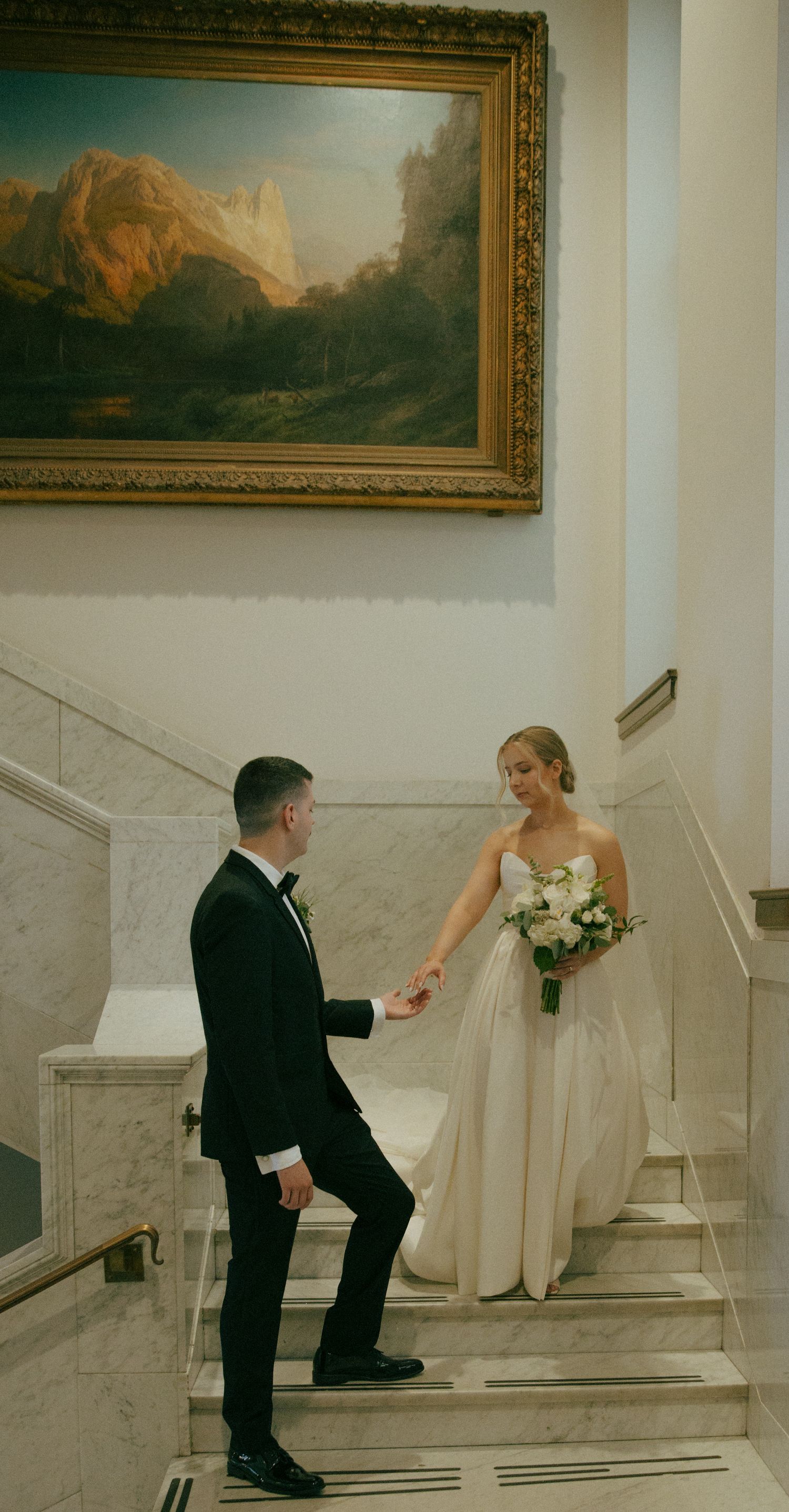 Elegant wedding photo on marble stairs with landscape painting in background.