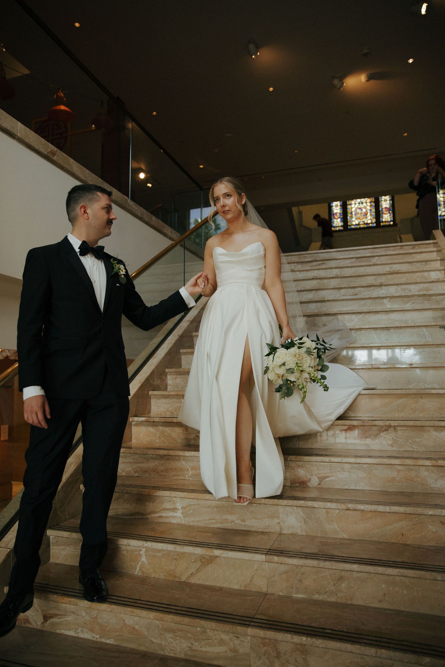 Couple in formal attire ascending elegant marble staircase.