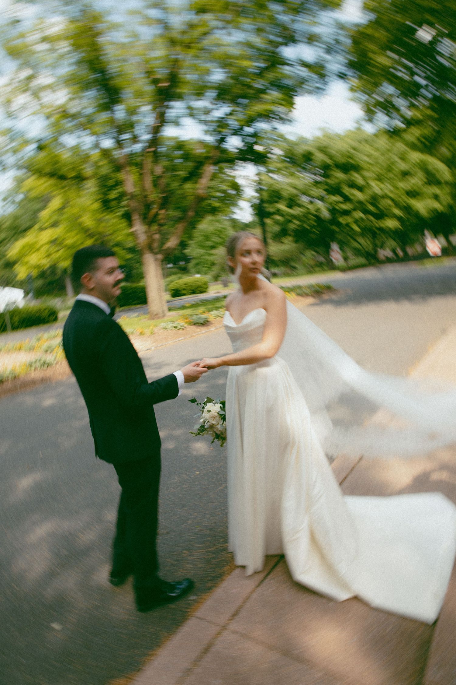 Artistic motion blur of couple in wedding attire on paved garden path.