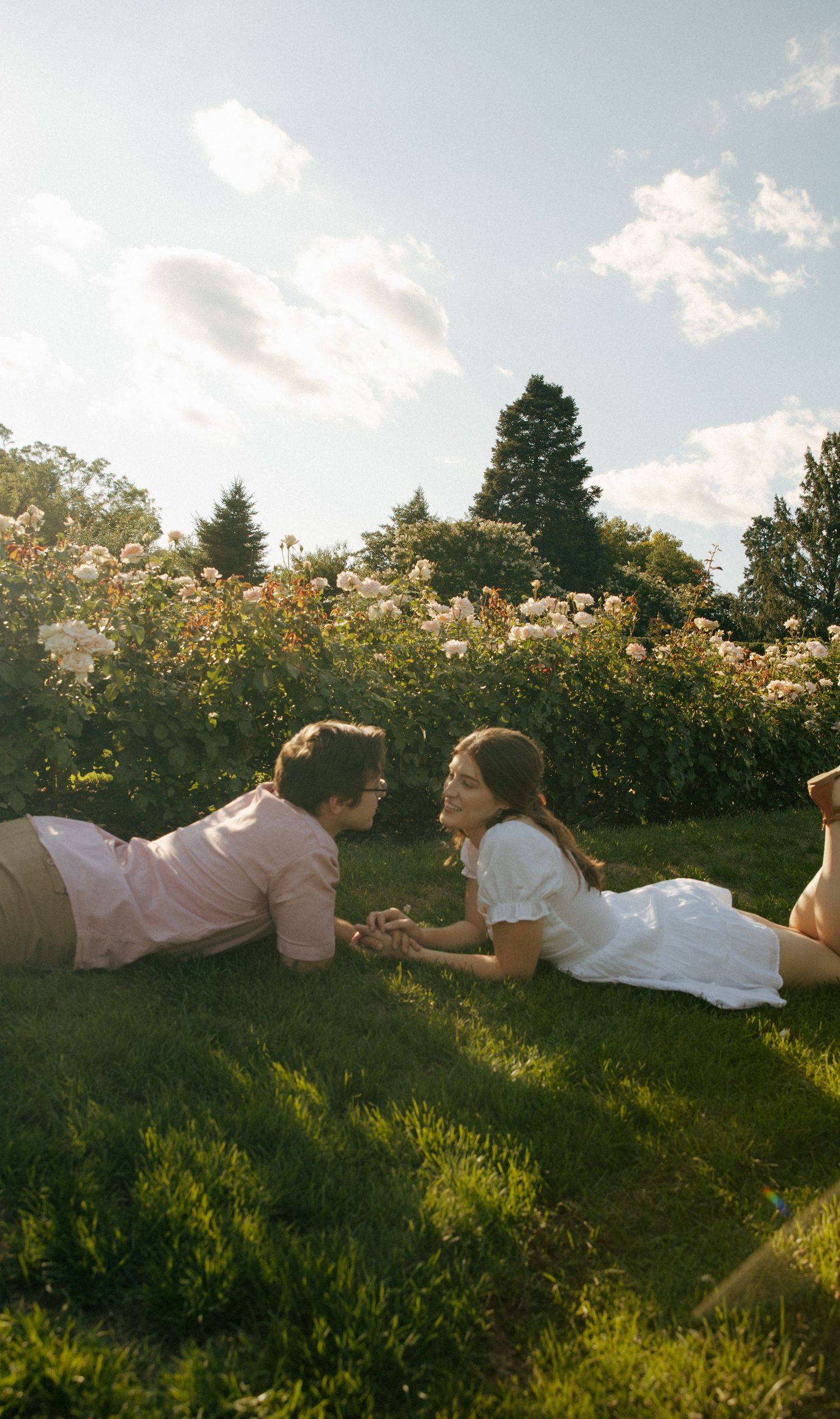 Couple laying on grass in garden during golden hour with roses in background.