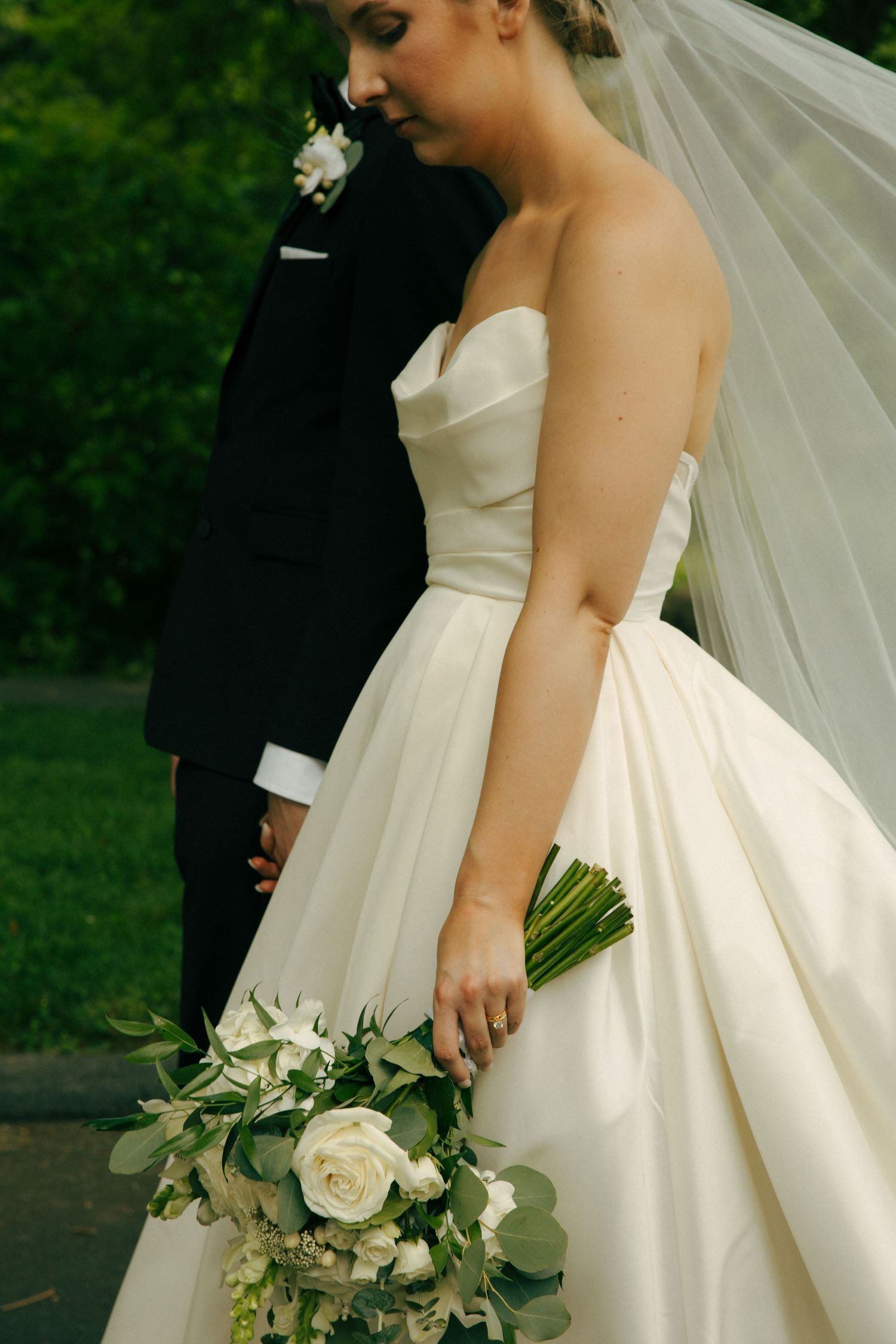 Elegant wedding dress details with white bouquet featuring roses and greenery.
