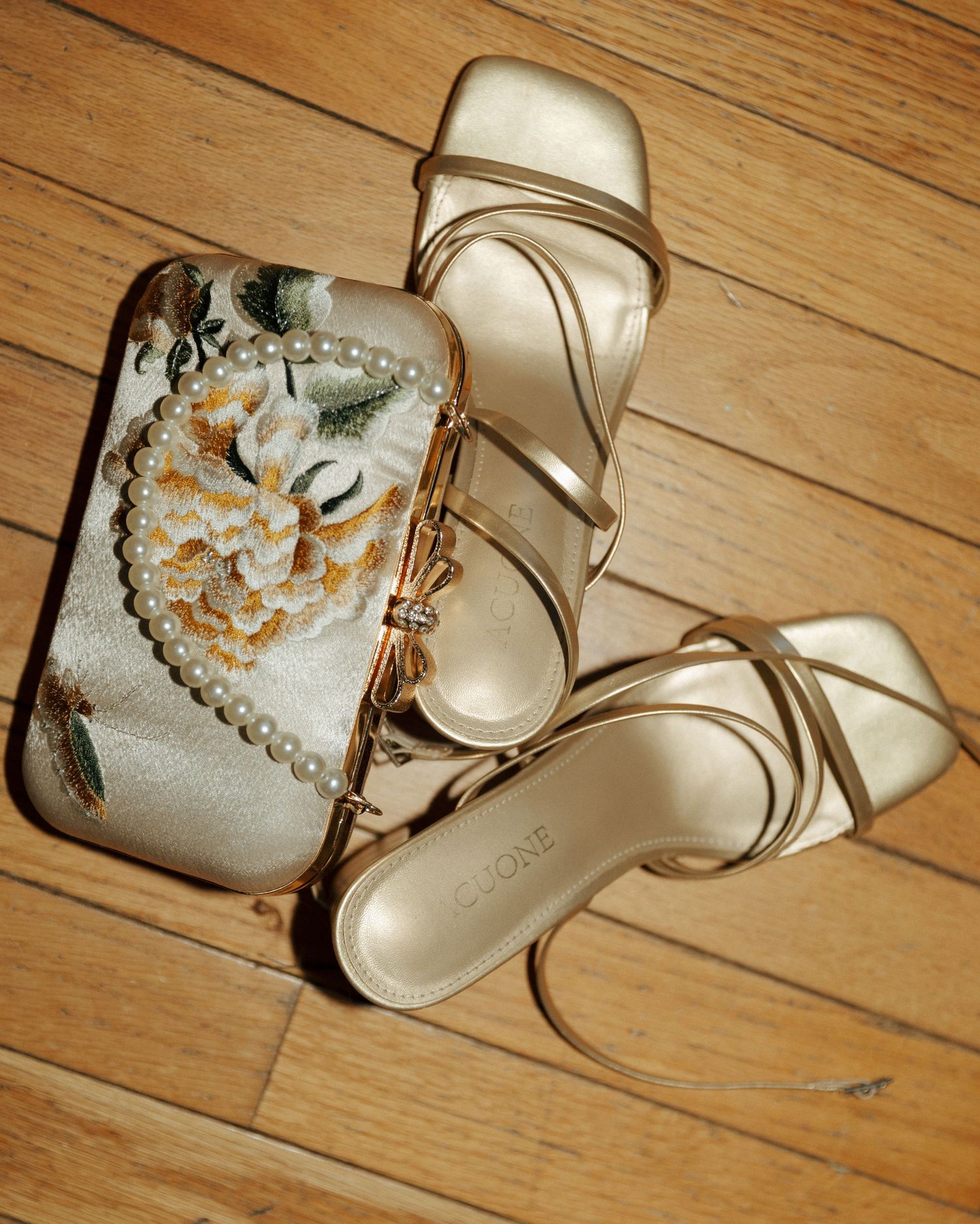 Elegant ivory bridal shoes and clutch with floral details displayed on hardwood flooring.
