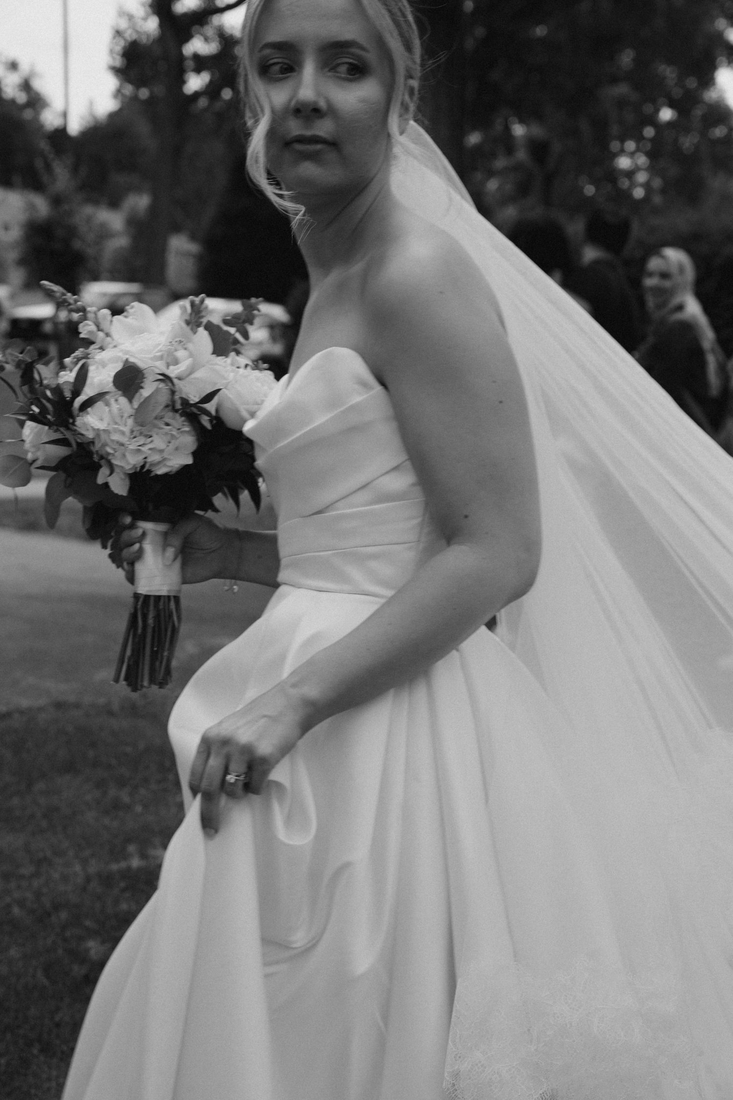Black and white portrait of bride holding bouquet in classic strapless wedding gown.