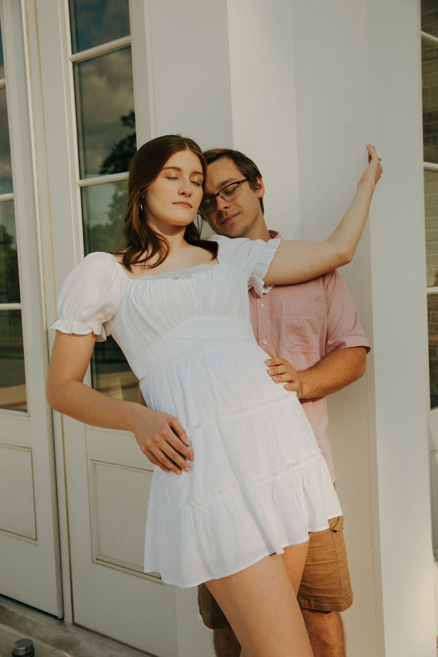 Romantic pose against white building exterior in afternoon sunlight.