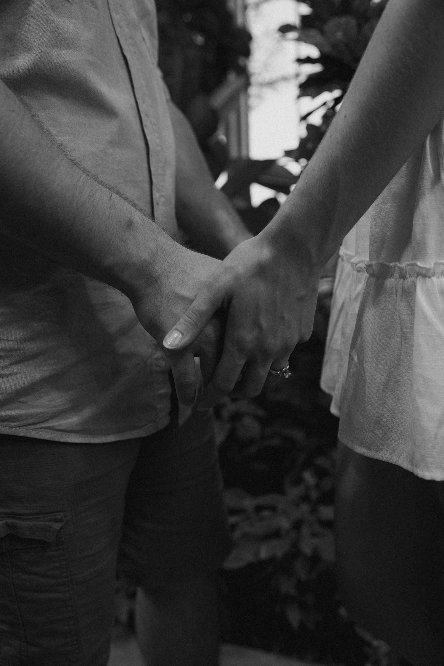 Black and white photo of two people holding hands intimately outdoors.