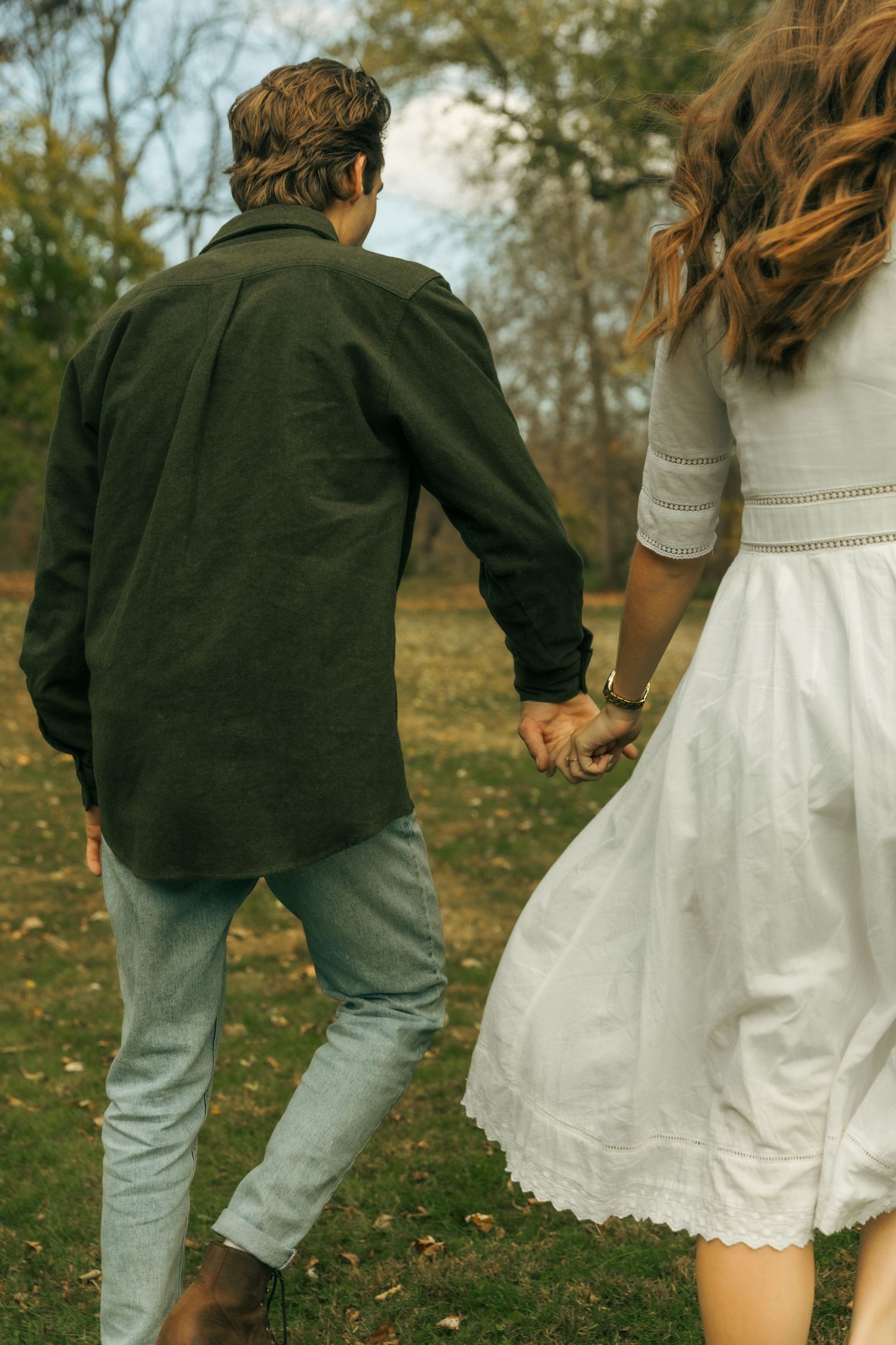 Walking couple holding hands from behind, showing casual and formal outfit contrast.