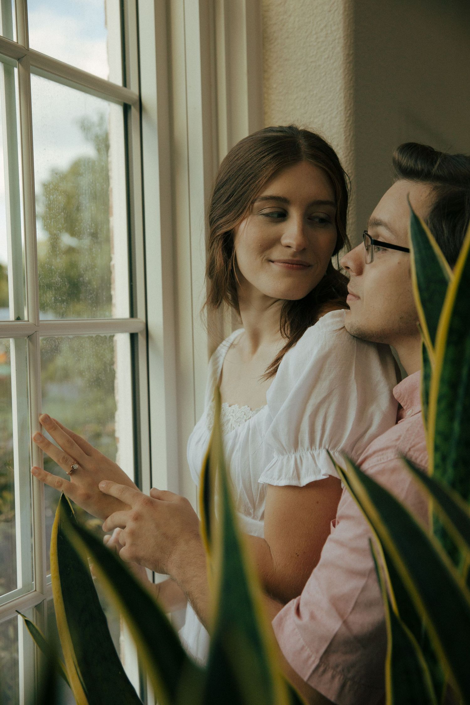 Intimate portrait of couple sharing tender moment by window with plants.