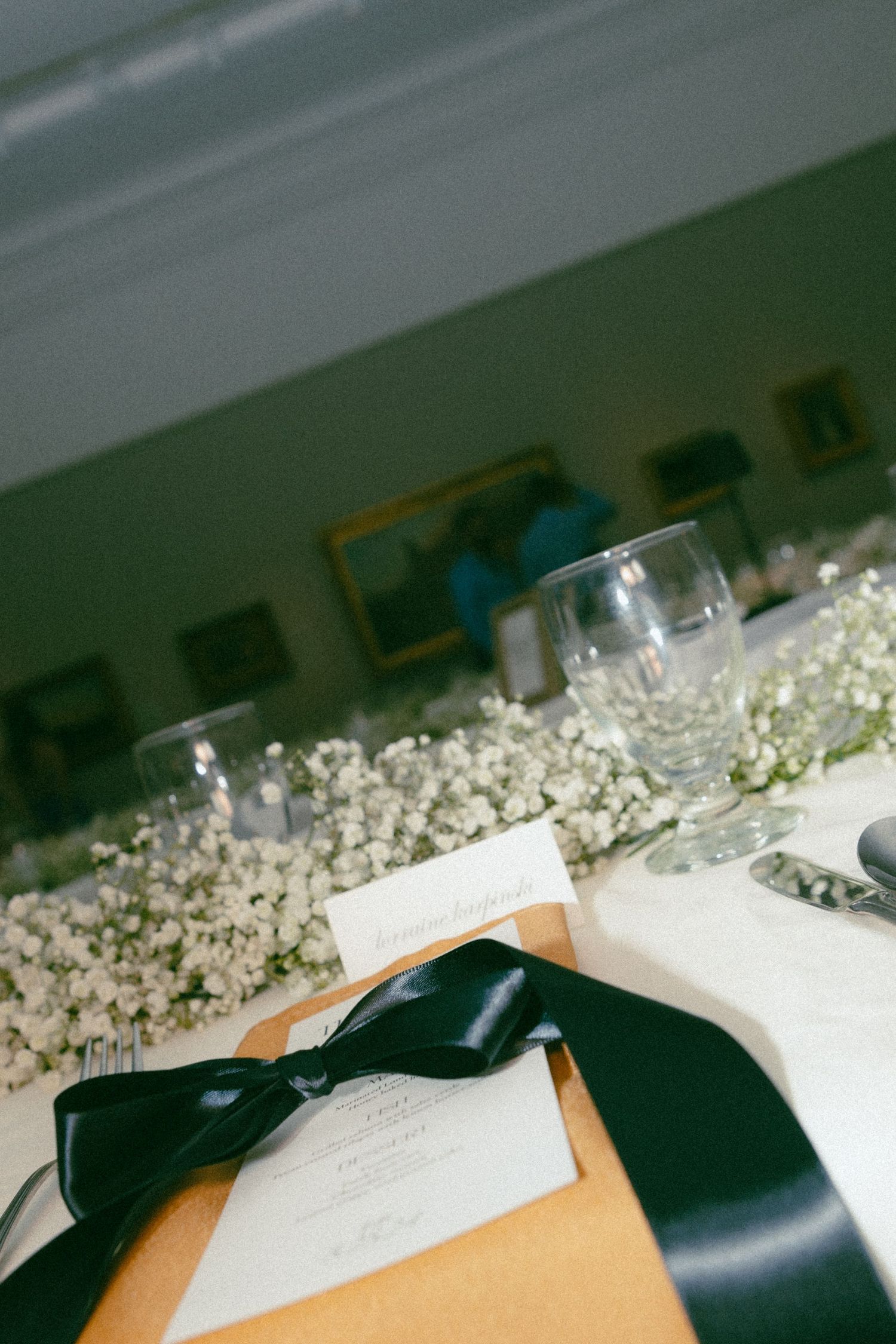 Wedding table setting with baby's breath flowers and a black bow tied invitation.