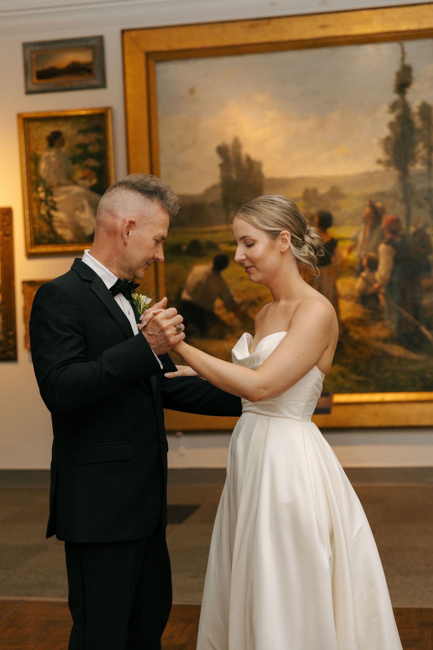 A couple shares an intimate dance moment in an art gallery surrounded by classic paintings.