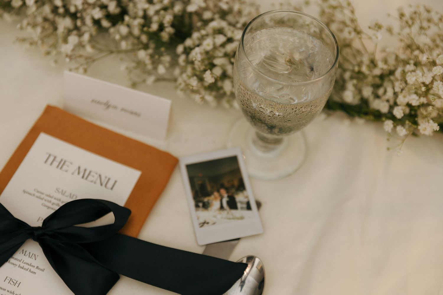 Wedding reception table setting with orange menu card and delicate floral decorations.