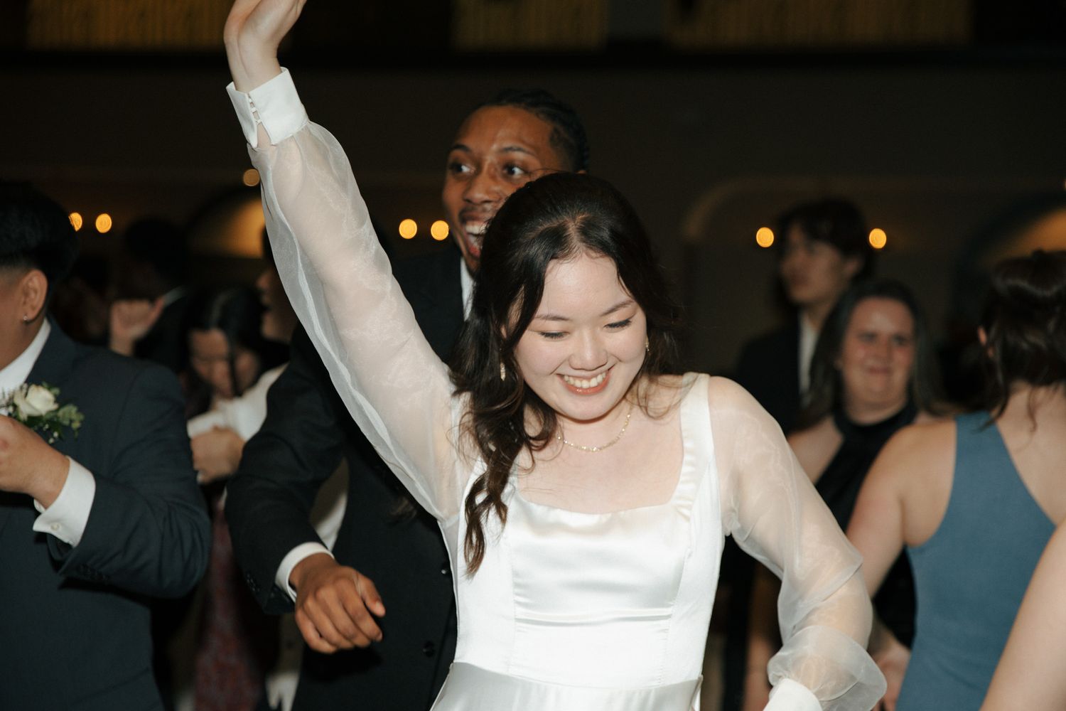 Joyful bride dancing with arms raised during wedding reception celebration.