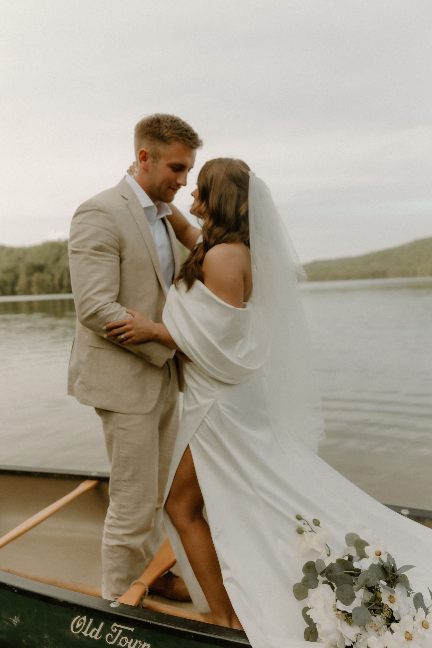 Wedding couple sharing a tender moment while standing in an old canoe on the water.