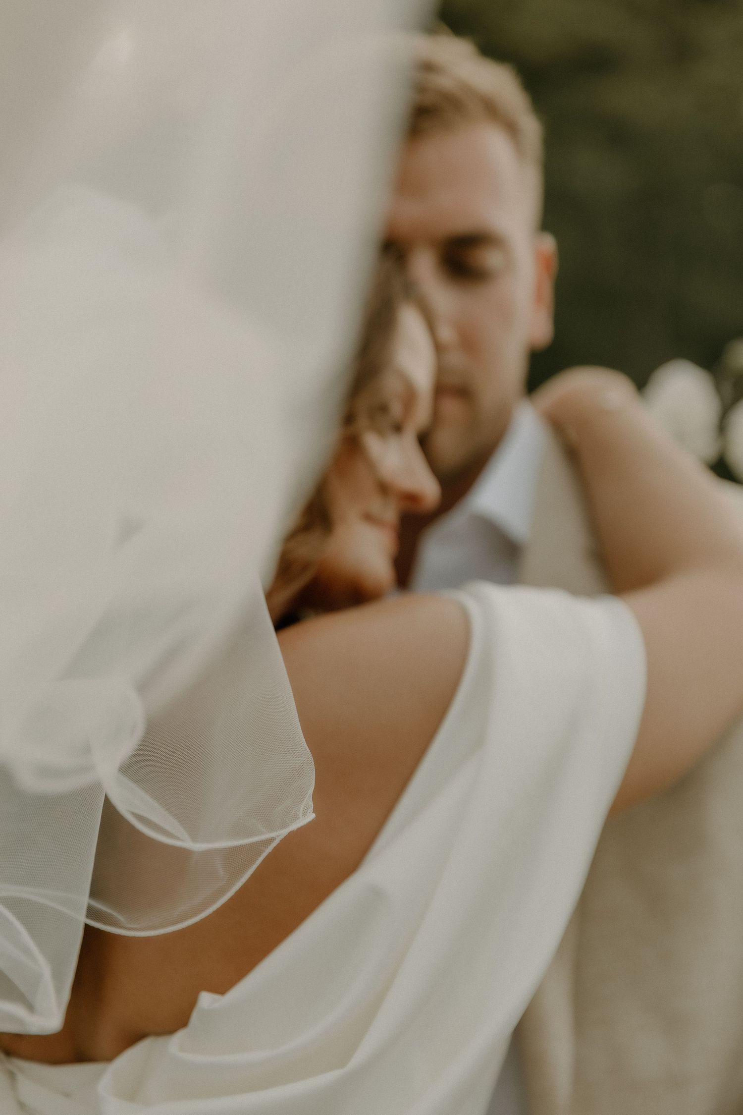 Close-up shot of newlyweds embracing with flowing white veil in soft lighting.