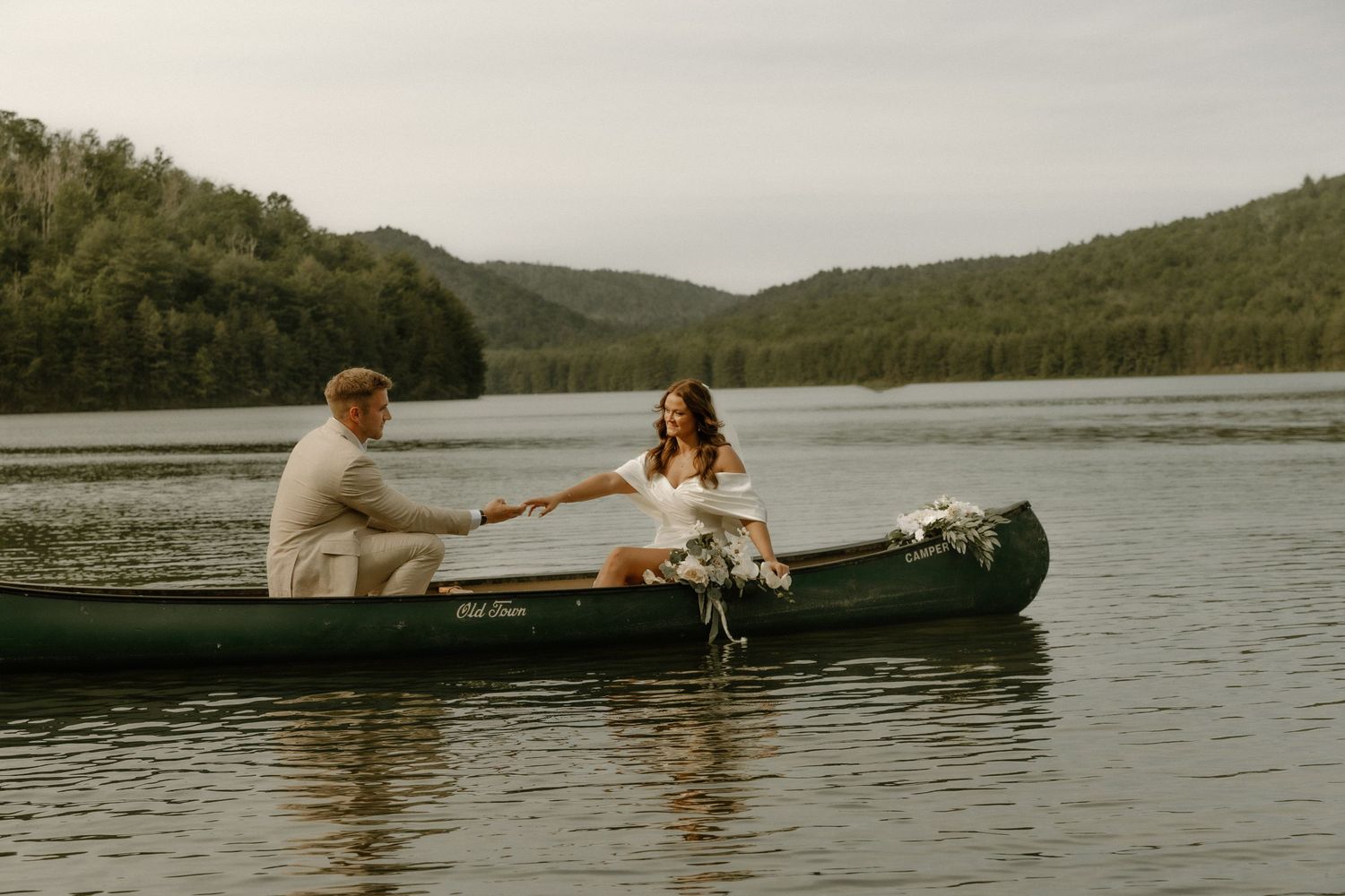 Wedding couple paddling together in a green canoe on a misty lake.