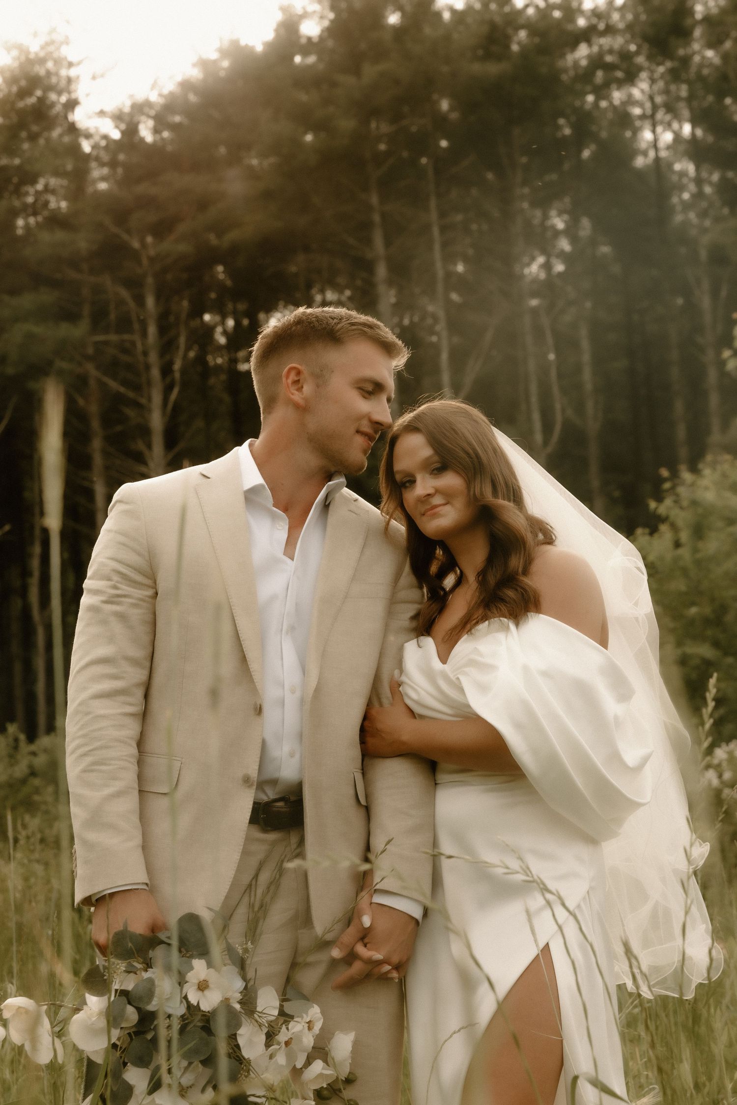 Intimate wedding portrait captured in a forest clearing with warm sunlight filtering through trees.