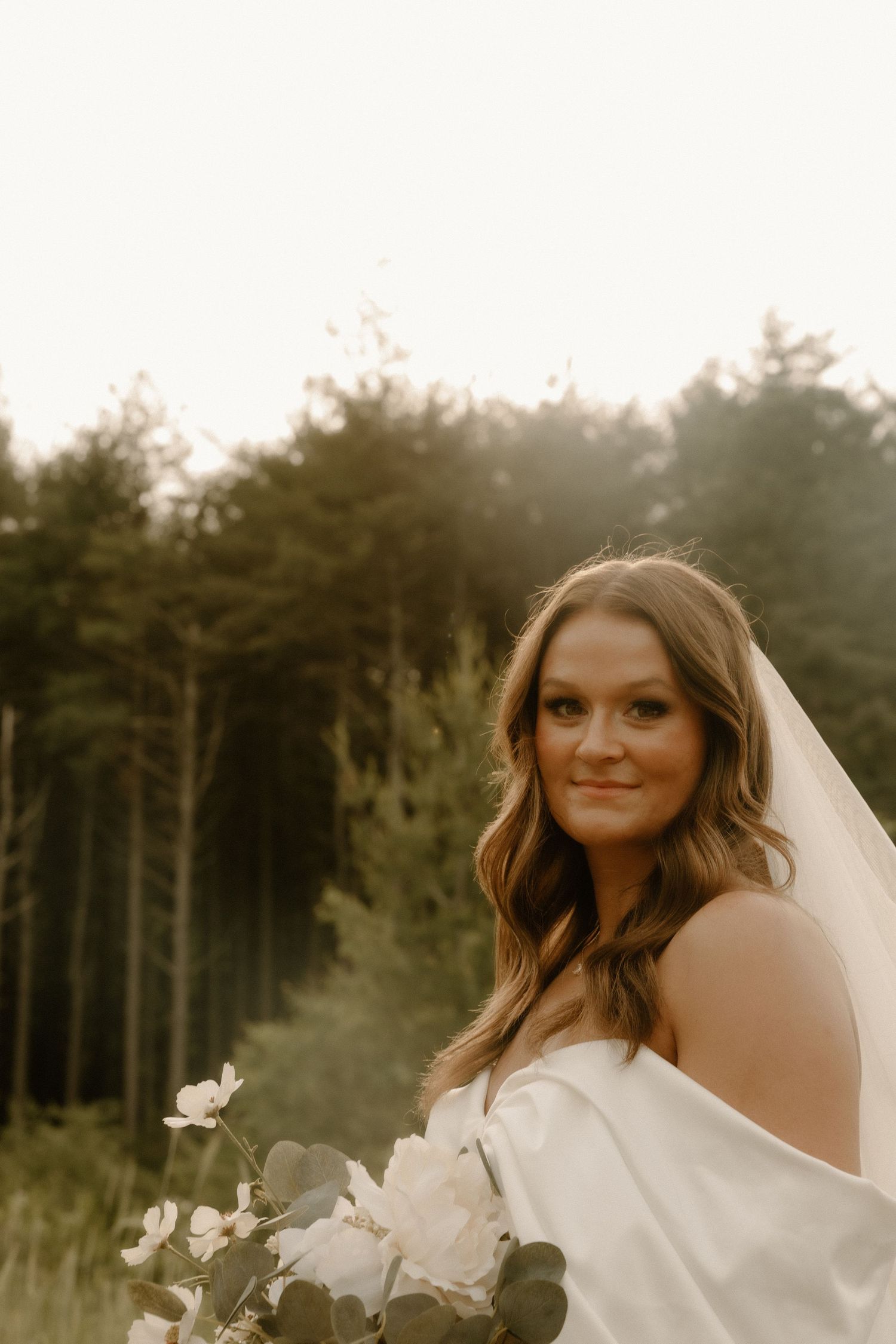 Ethereal bridal portrait with forest backdrop and white floral bouquet.