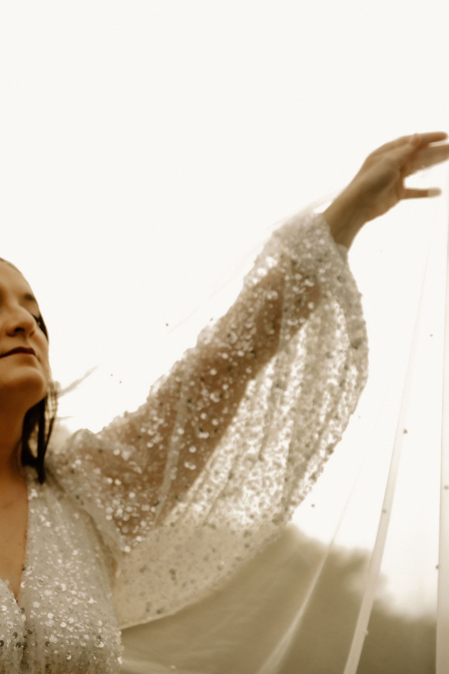 Ethereal bridal portrait showing sparkly sequined dress sleeve against bright backlight.