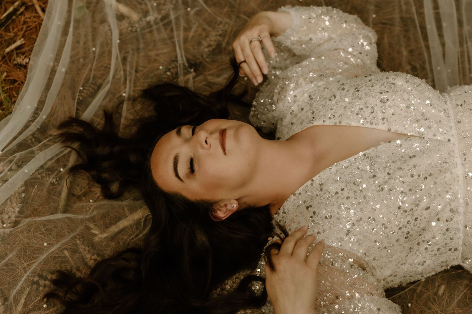 Bride in a sparkling sequined wedding gown lying down with closed eyes in a dreamy pose.