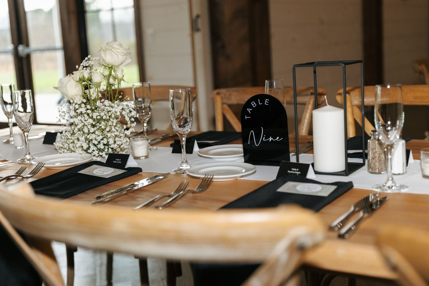 Elegant wedding table setting with black menus, baby's breath flowers, and white candles on a wooden round table.
