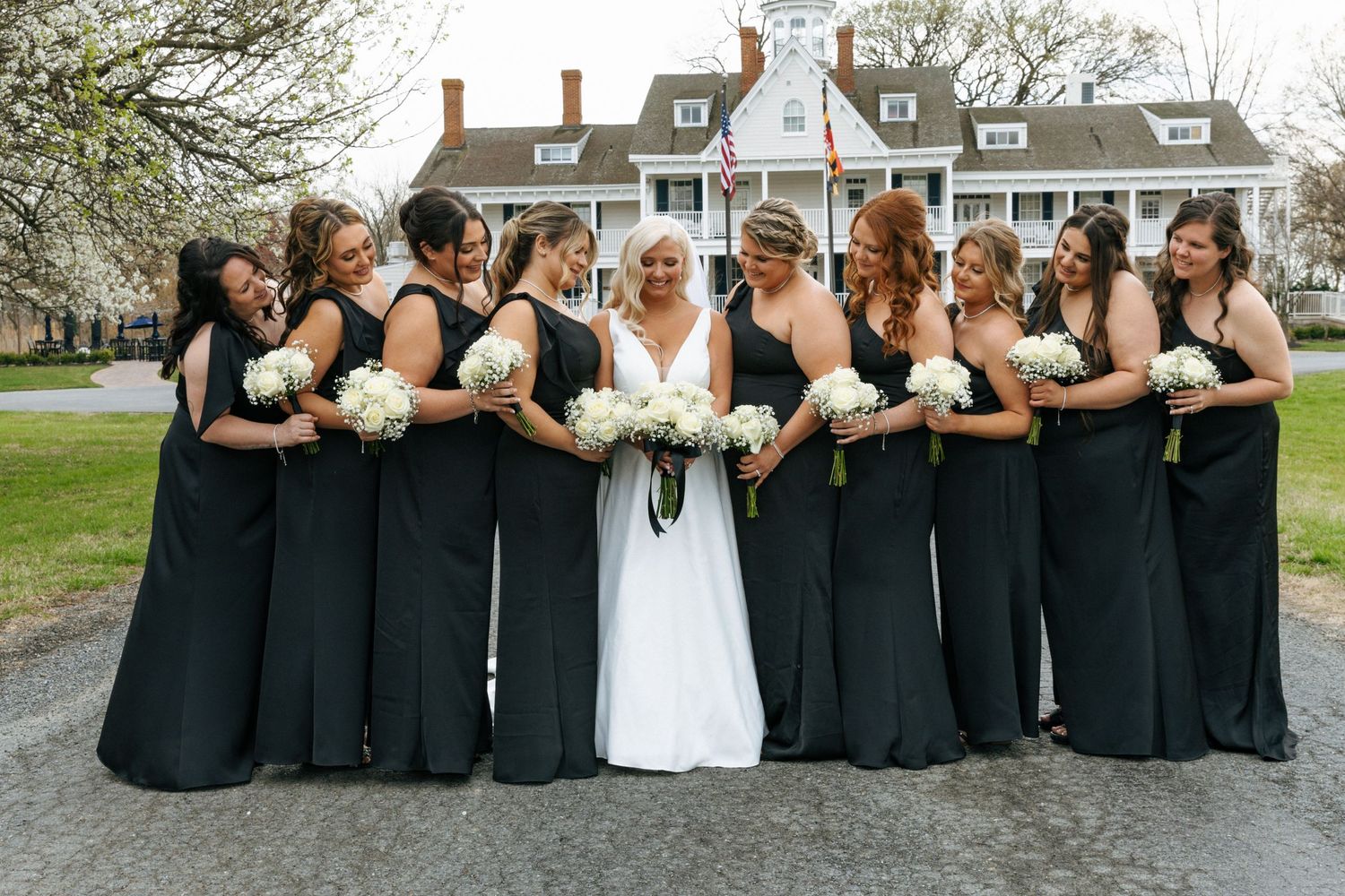Wedding party poses together outdoors, wearing elegant black bridesmaid dresses and holding white bouquets.