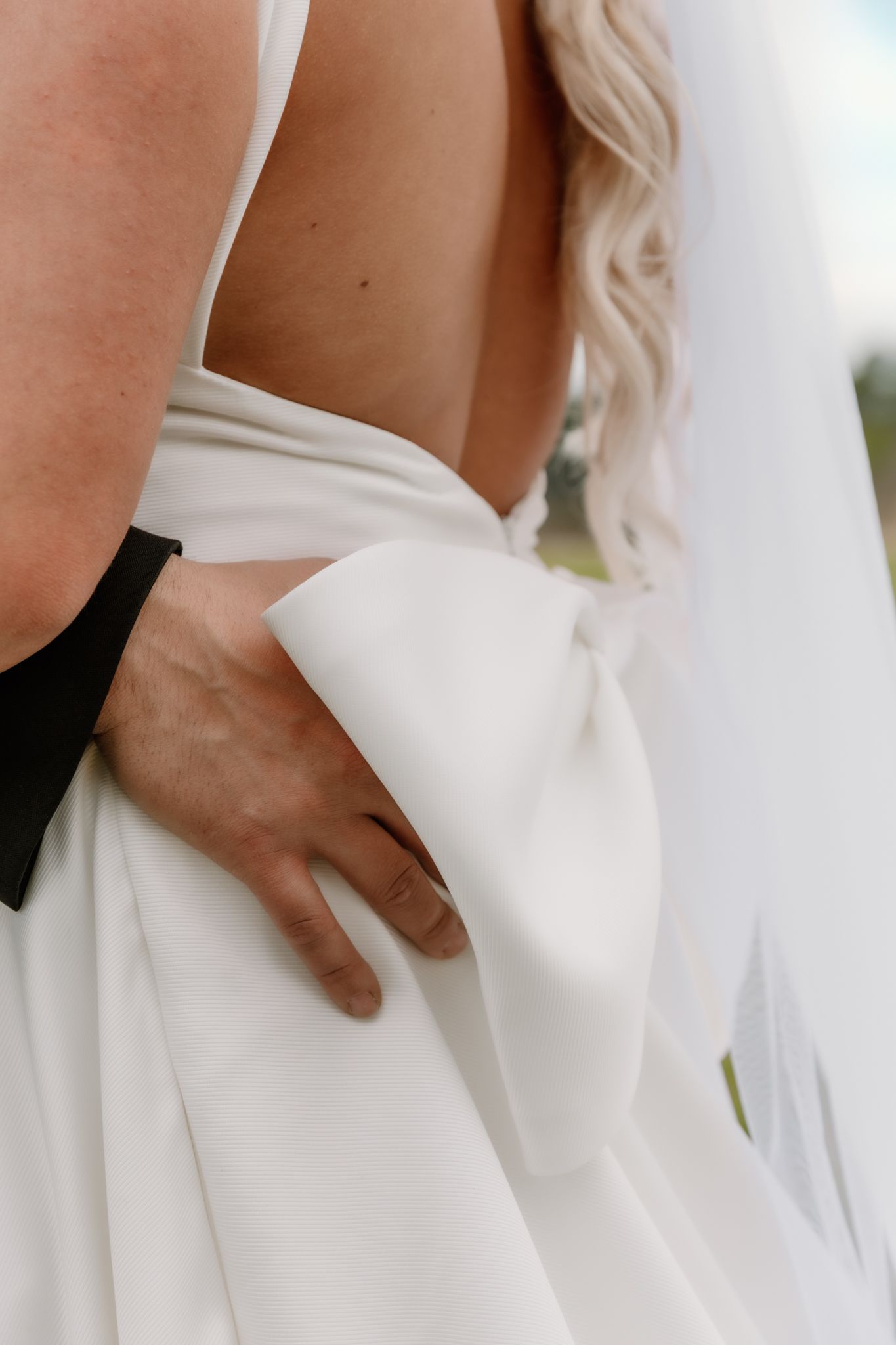 Close up of hand holding the fabric of a white wedding dress, showing elegant pleats and draping details.