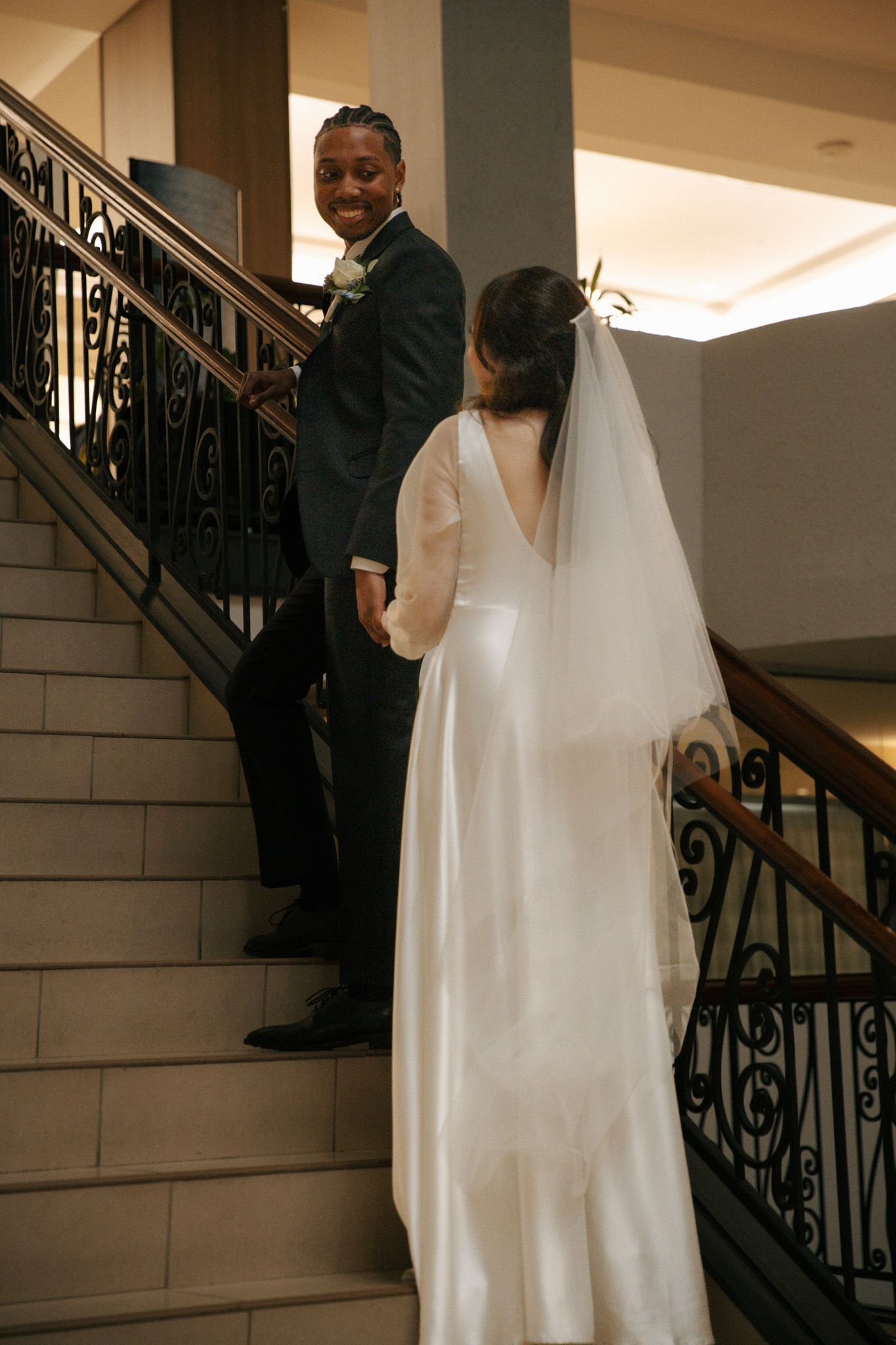 Bride and groom pose on an elegant staircase with ornate iron railings.