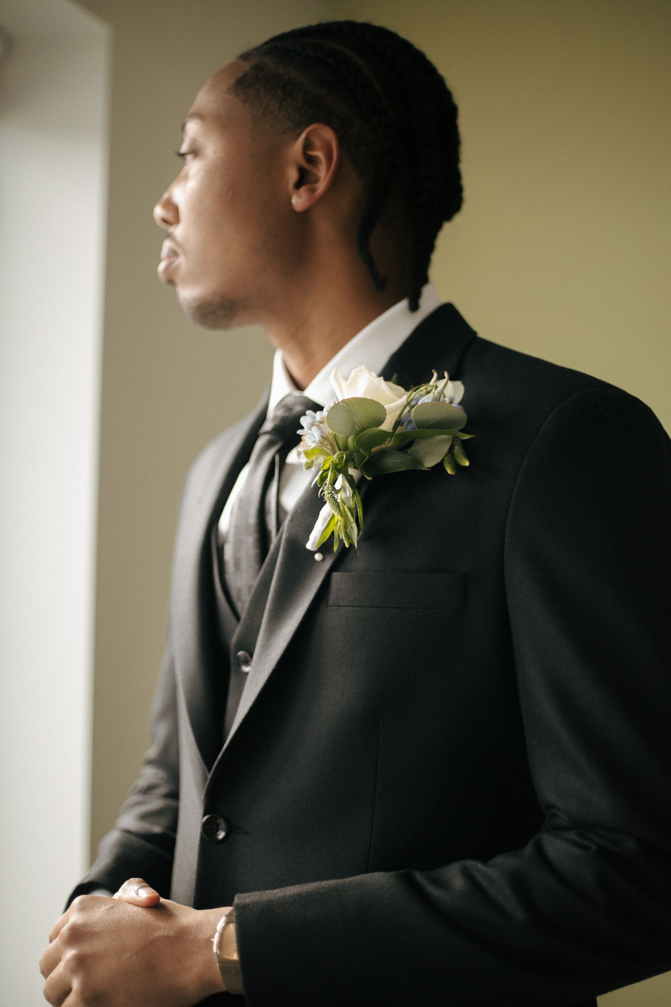 Groom in classic black tuxedo with white boutonniere looking to the side.