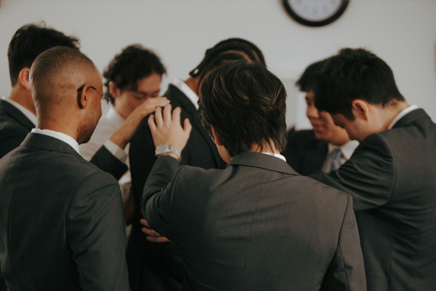 Group of groomsmen bowing heads in prayer or reflection before wedding ceremony.