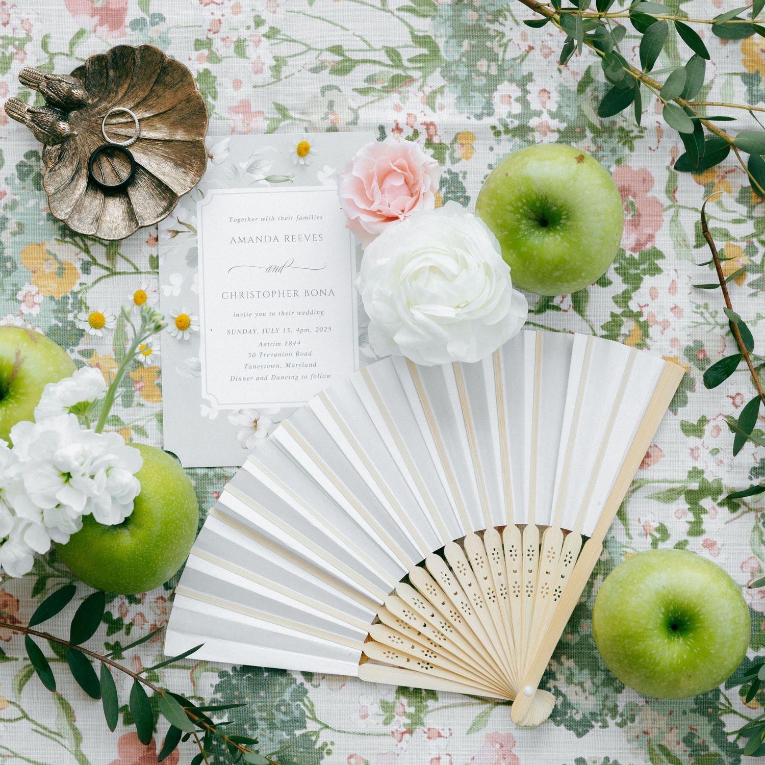 White paper fans and green apples arranged with floral decor and greenery on a delicate floral print background.