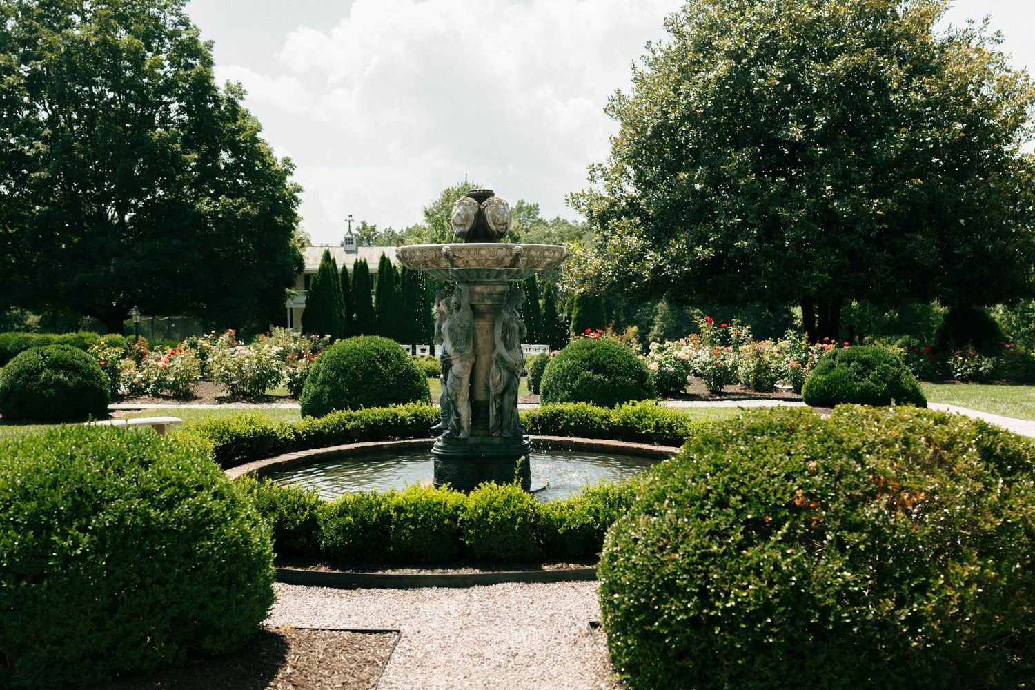 Elegant garden fountain centerpiece surrounded by manicured hedges and landscaping in a formal garden setting.