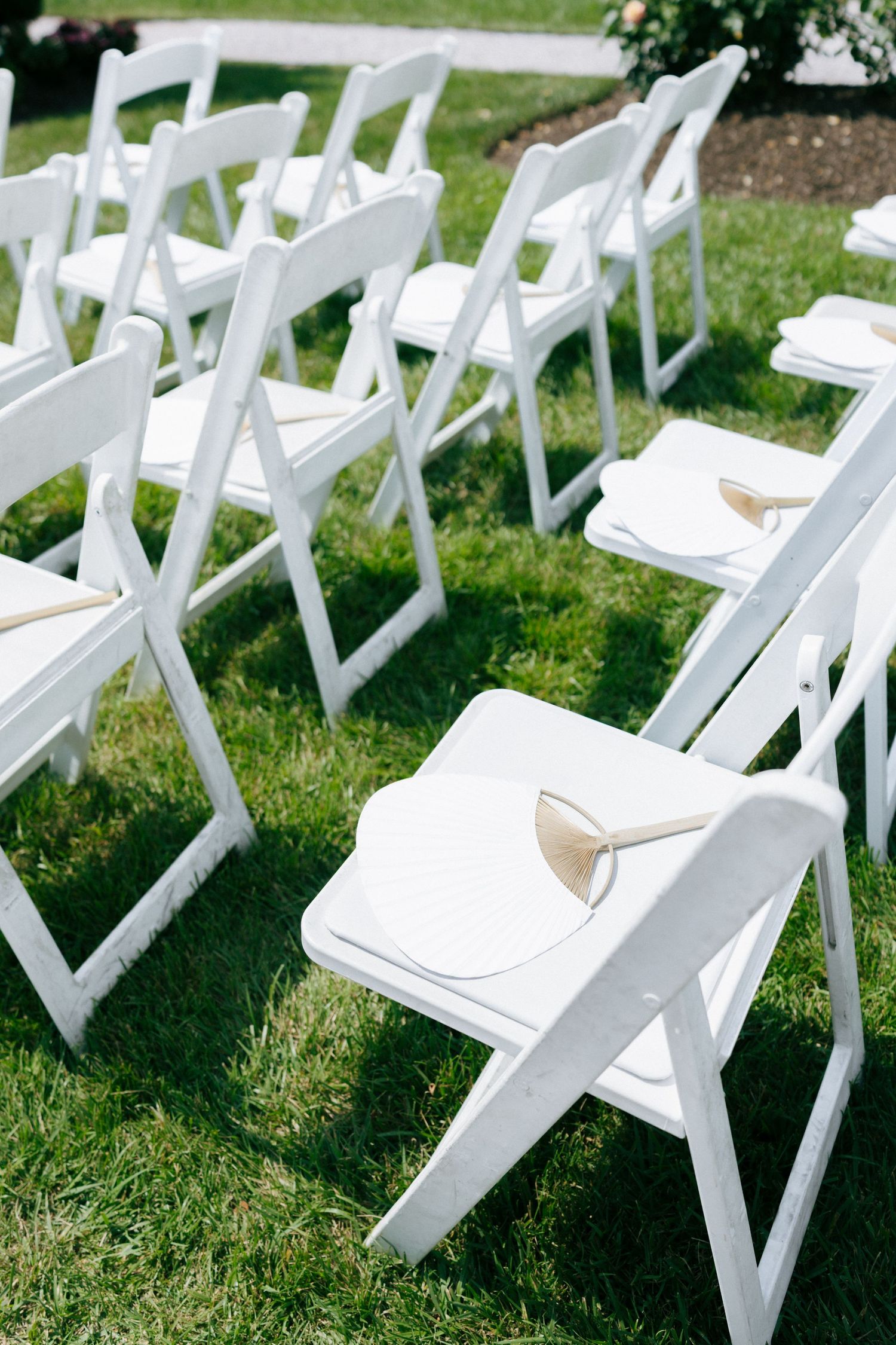 White folding chairs arranged in rows on a grassy lawn for an outdoor wedding ceremony.