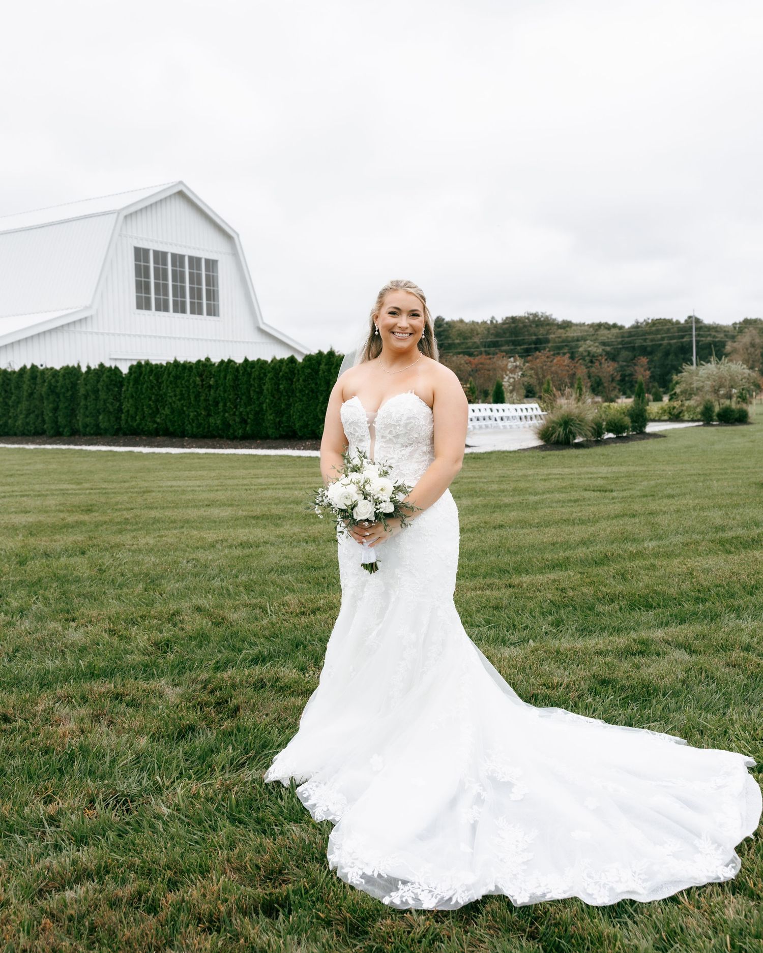 A scenic wedding portrait series featuring a white barn venue with rolling green hills and a flowing lace wedding gown.