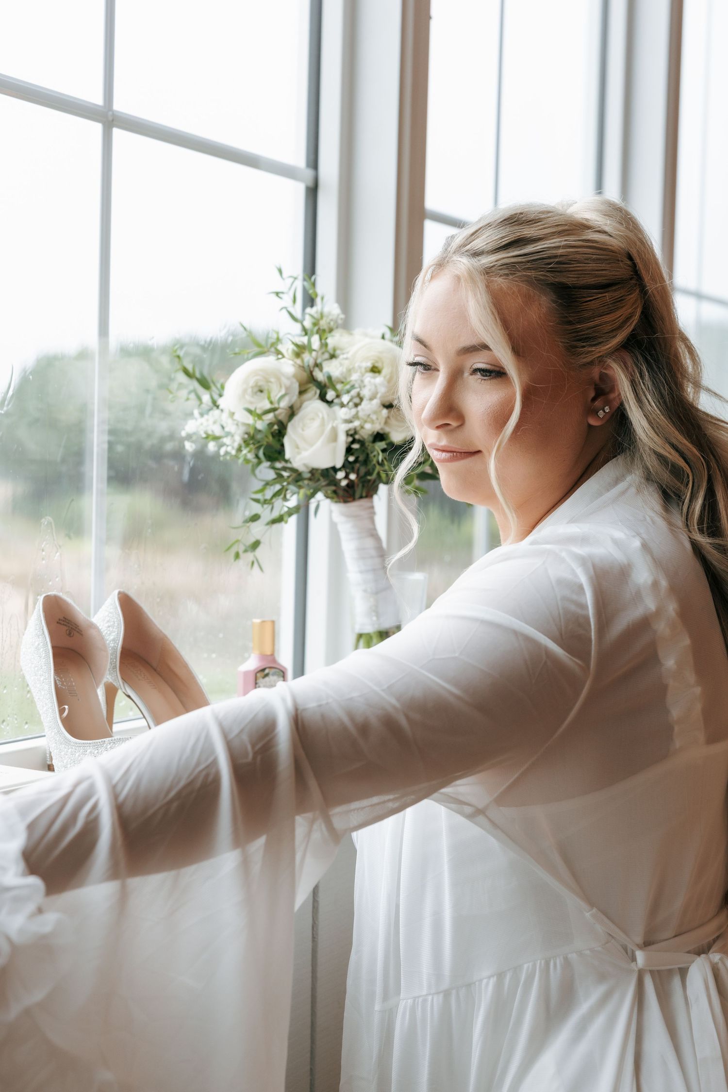 A series of getting ready photos showing someone in white attire looking out large windows with floral bouquets.