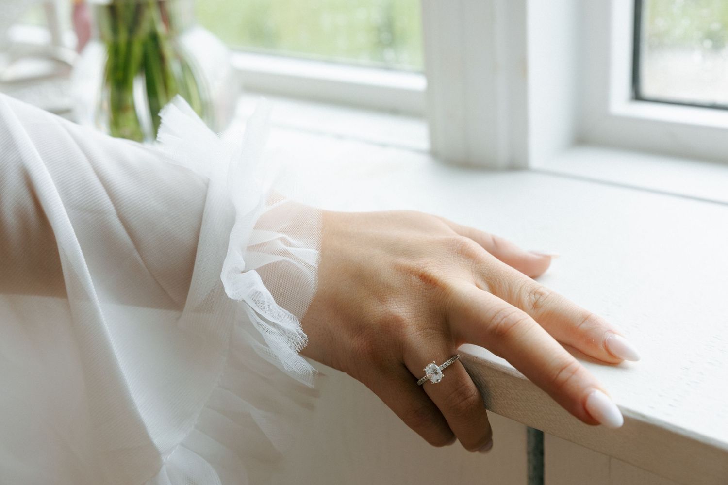 Woman's hands with red manicure gently resting on a white windowsill in natural daylight.