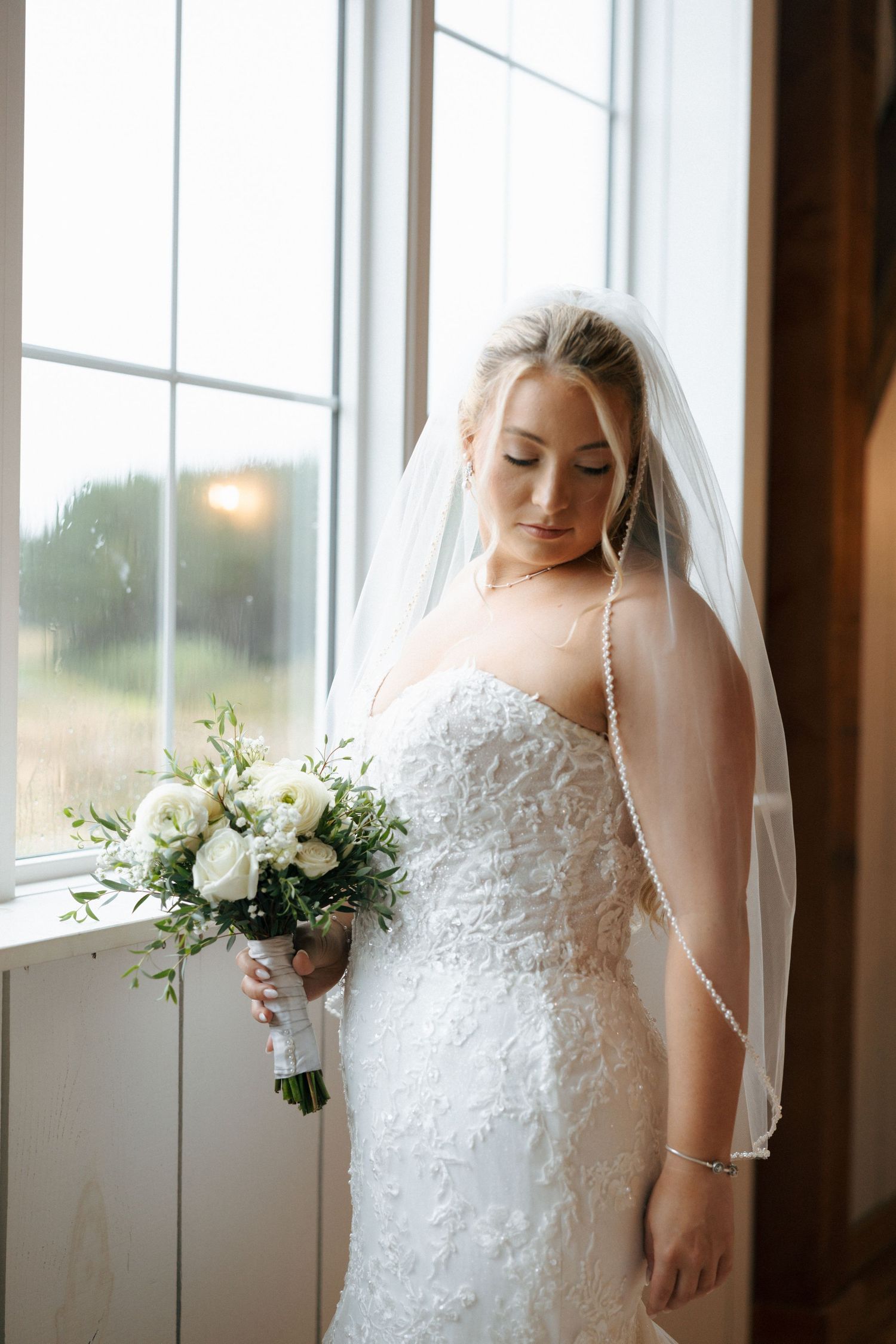 Elegant bridal portraits in white lace gown by sunlit windows with delicate floral bouquet.