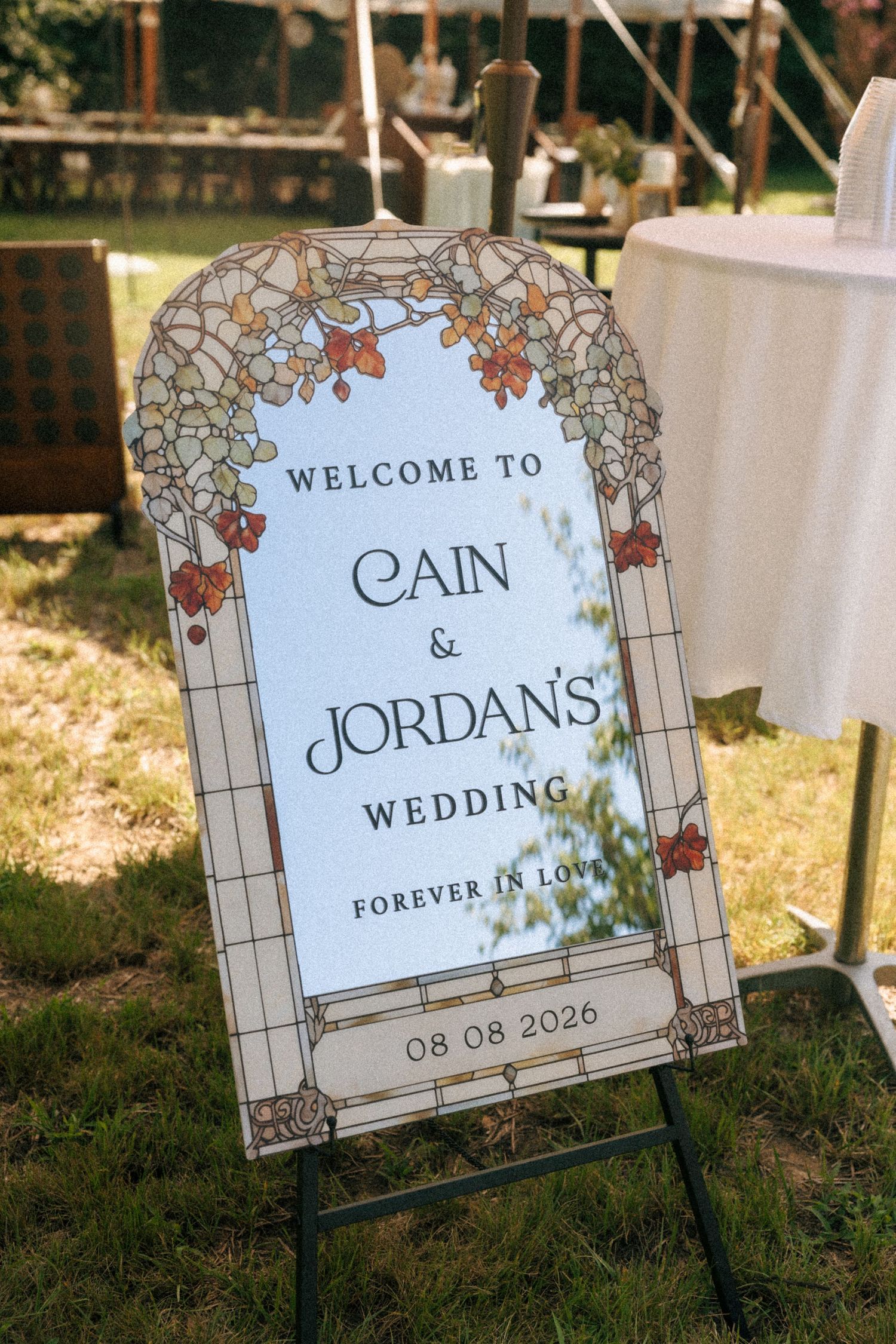 Art nouveau wedding welcome sign for Cain and Jordan's wedding on 08.08.2026, featuring floral arch design on green lawn.
