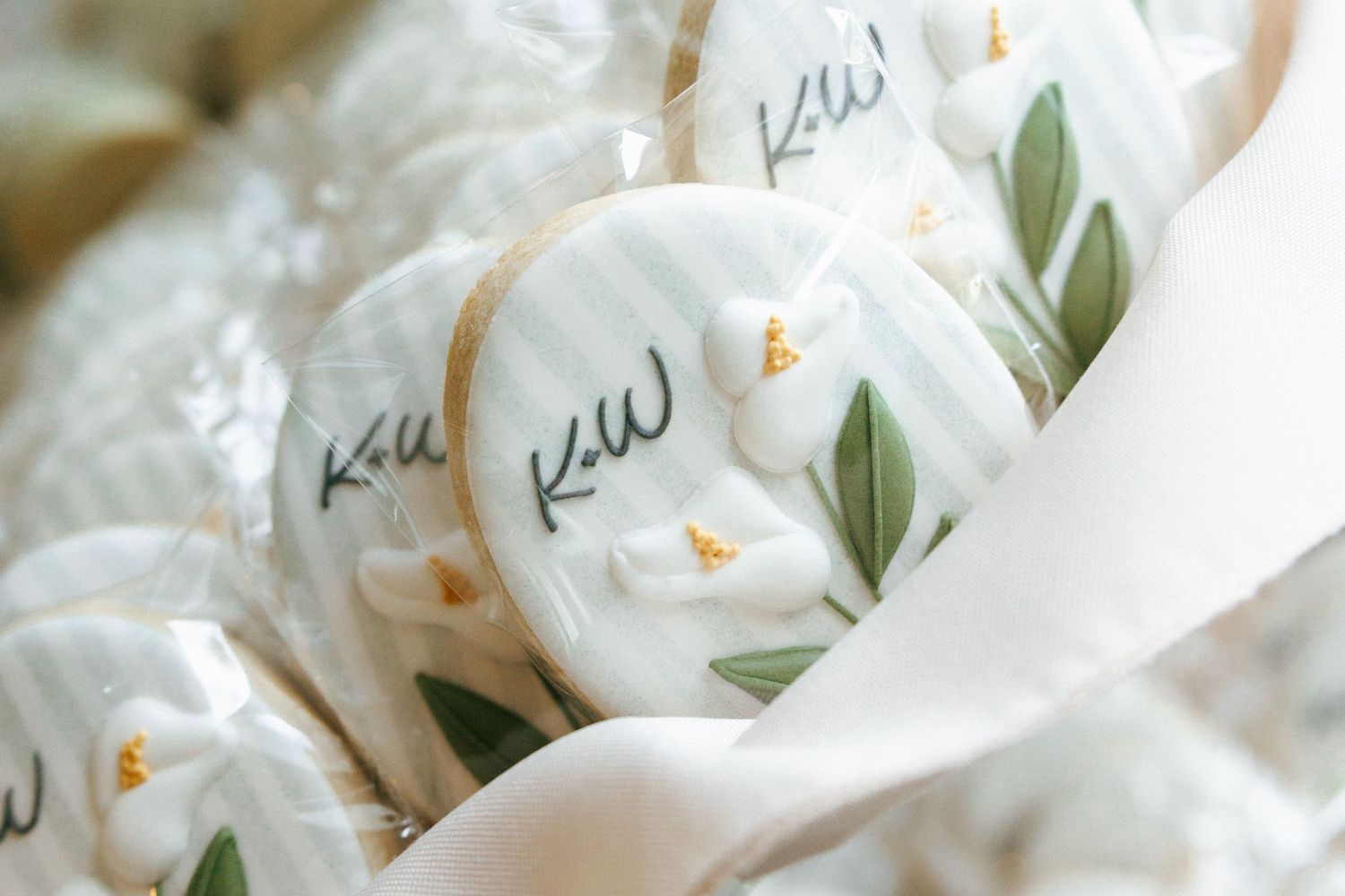 White royal icing wedding cookies with KW monogram and green floral design, wrapped in ribbon.