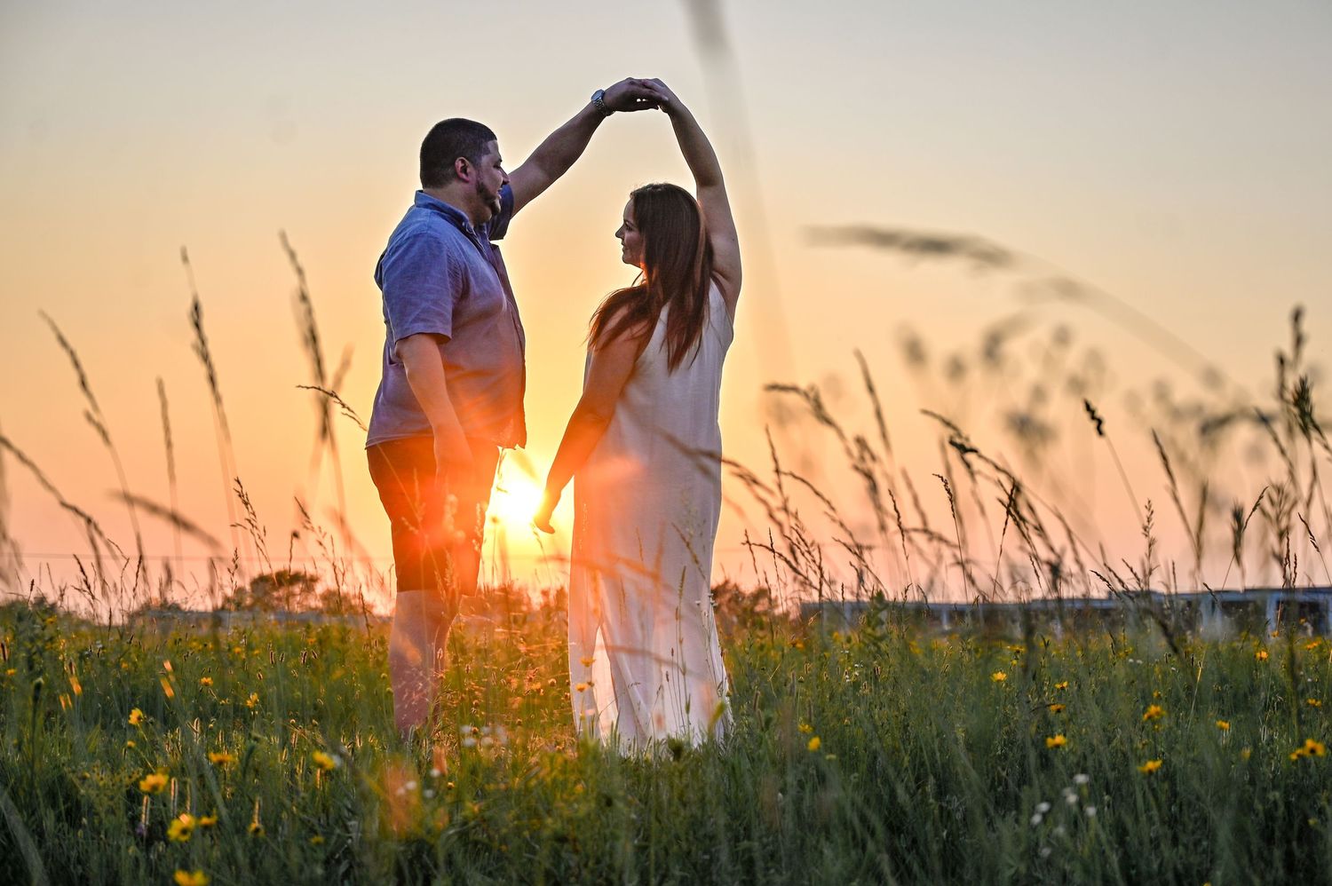 A couple dances in a wildflower meadow at sunset creating a romantic silhouette.