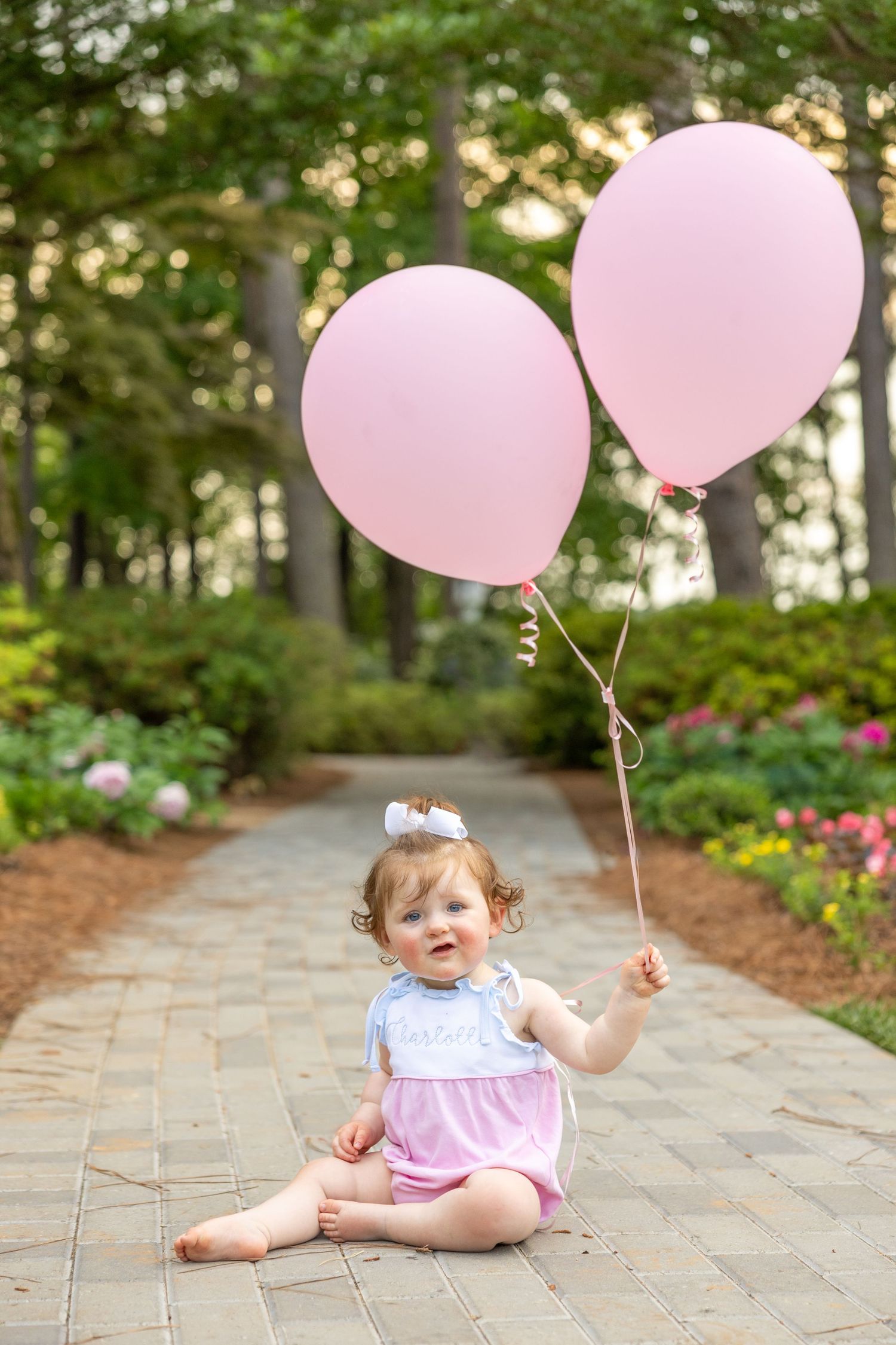 A redhead baby girl sits and holds 2 balloons at her 1st birthday photo session in Raleigh, NC.