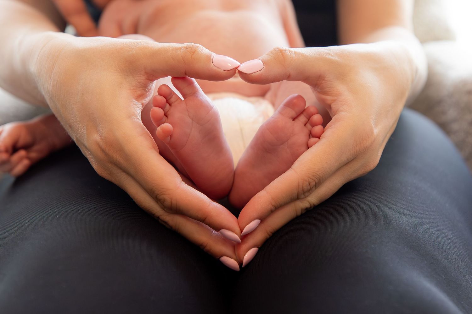 A mother's hands make a heart shape around her baby's feet - Family Photography