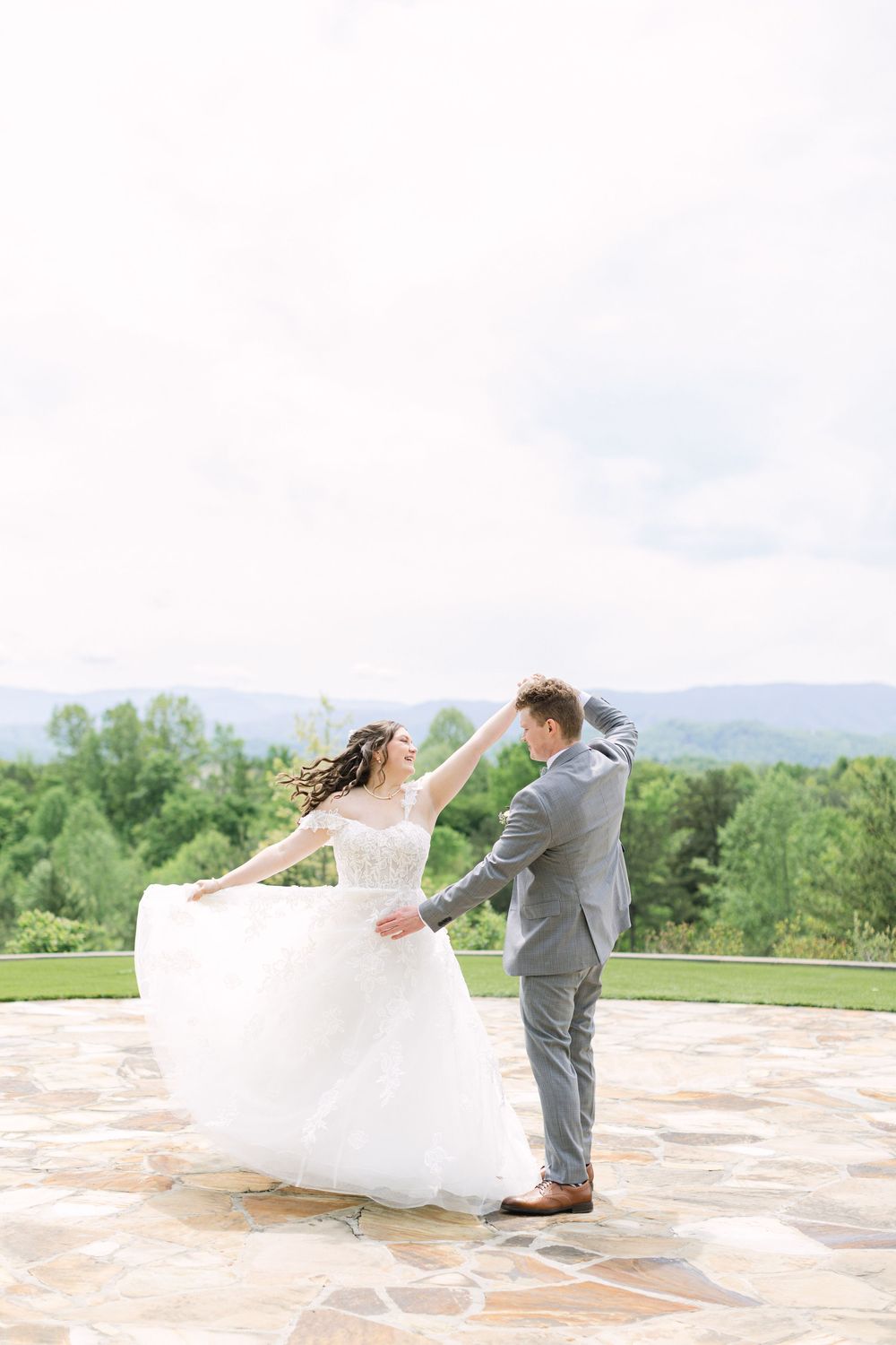 Bride and groom dancing outdoors on stone patio with lush green mountains in the background on their wedding day.