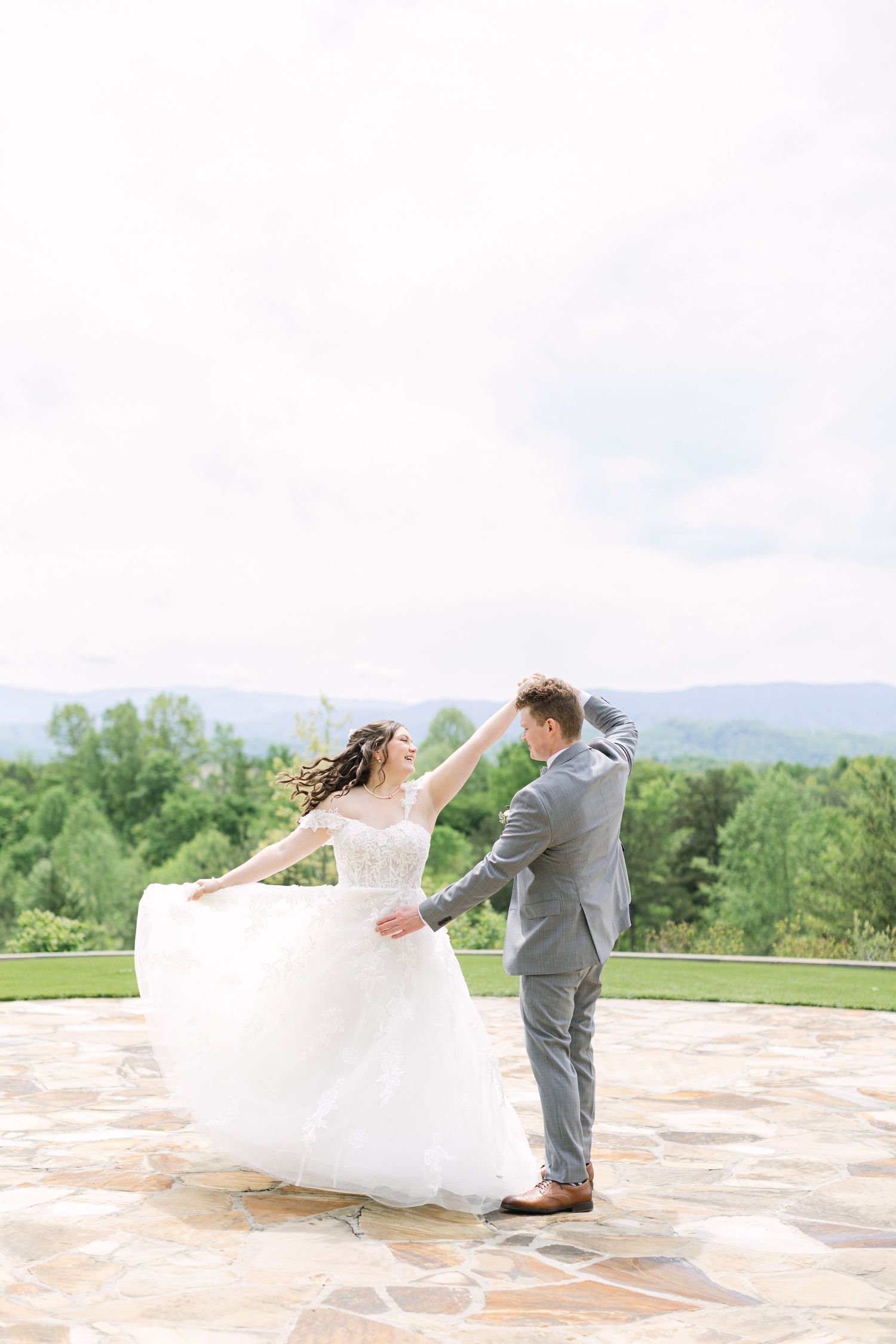 Bride and groom dancing outdoors on stone patio with lush green mountains in the background on their wedding day.