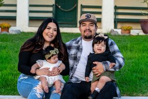 Family relaxes on green lawn in front of Spanish colonial architecture.