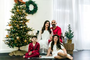 Holiday family portraits with Christmas tree and festive green wreath decorations in background.