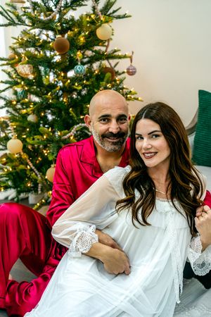Intimate Christmas portraits with couple in contrasting red and white outfits by decorated tree.