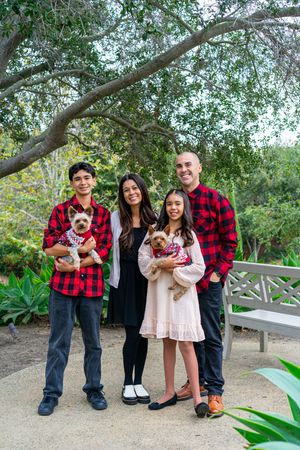 A family wearing red plaid and casual attire poses together on a garden path surrounded by lush greenery.